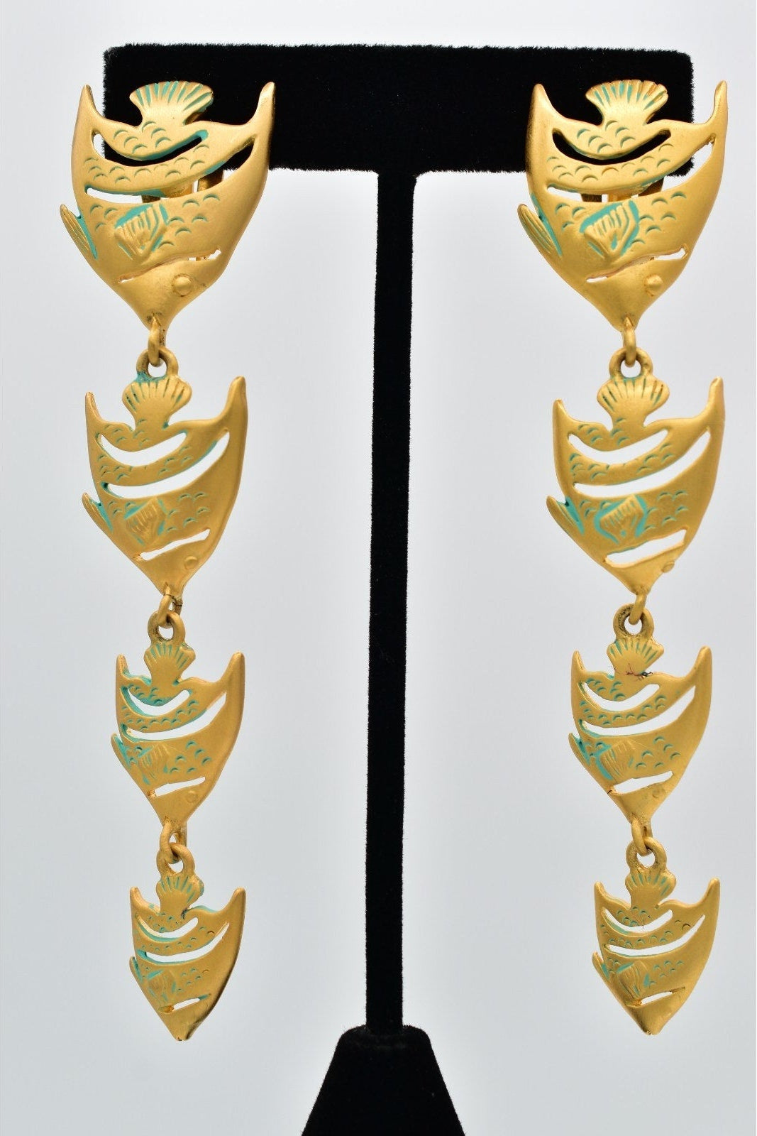 Gold and green Givenchy fish-shaped earrings on a black earring stand against a white background