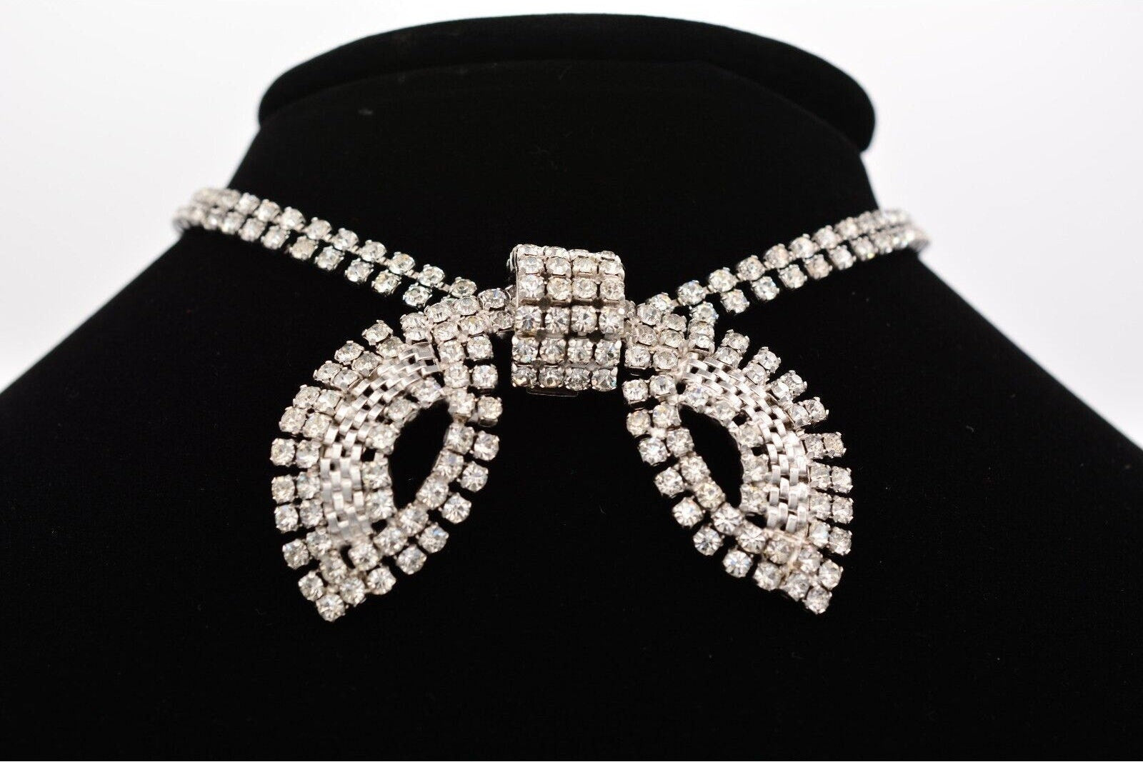 Silver choker necklace with intricate design on a black stand against a white background