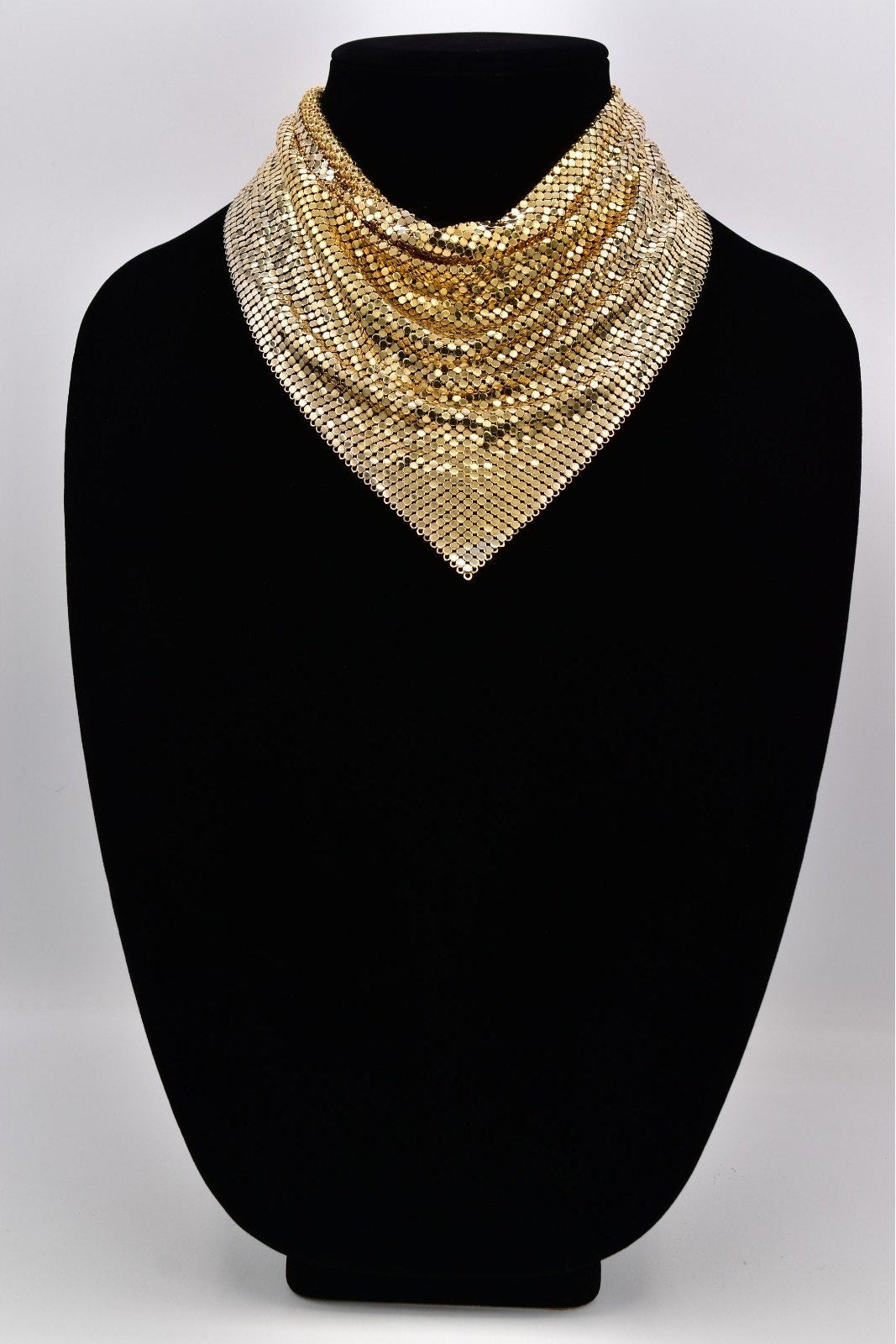 Gold beaded necklace on a black mannequin against a white background