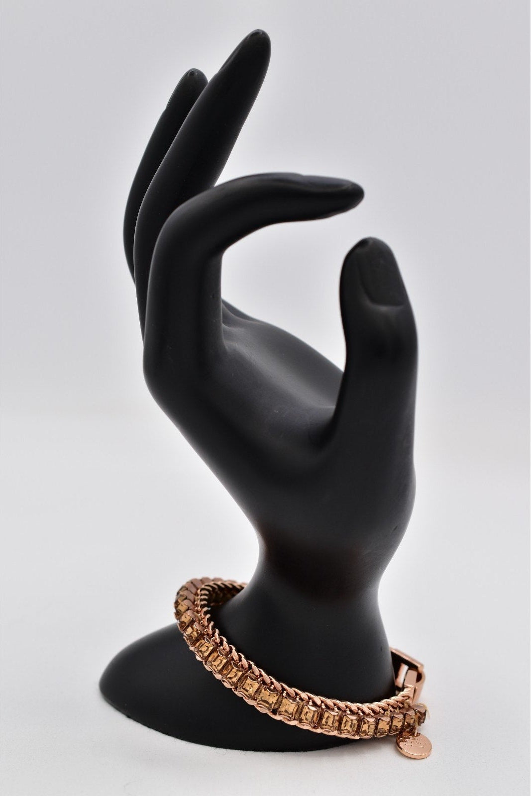 Black mannequin hand with a gold bracelet on a light gray background