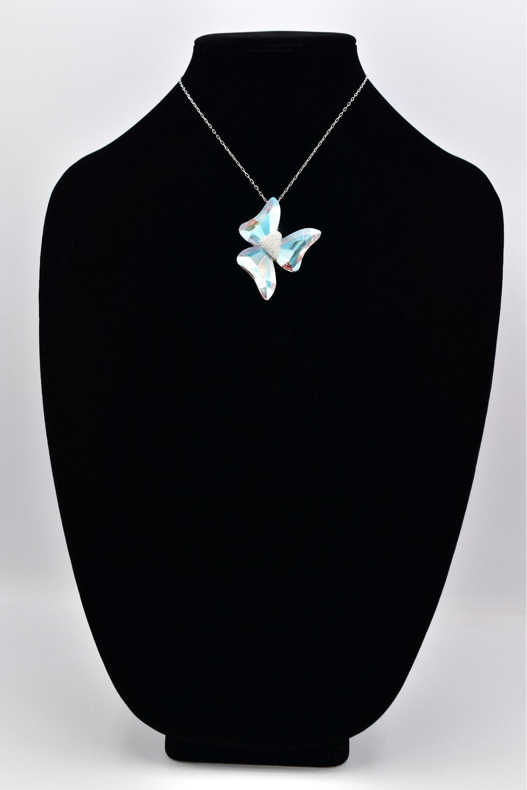 A silver butterfly pendant necklace with iridescent blue and white mother-of-pearl wings, displayed on a black velvet jewelry bust against a light gray background.