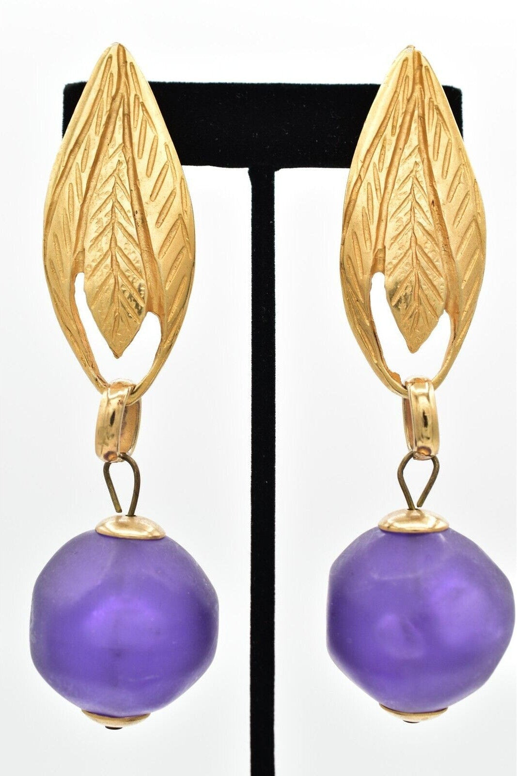Gold leaf earrings with purple beads on a black stand