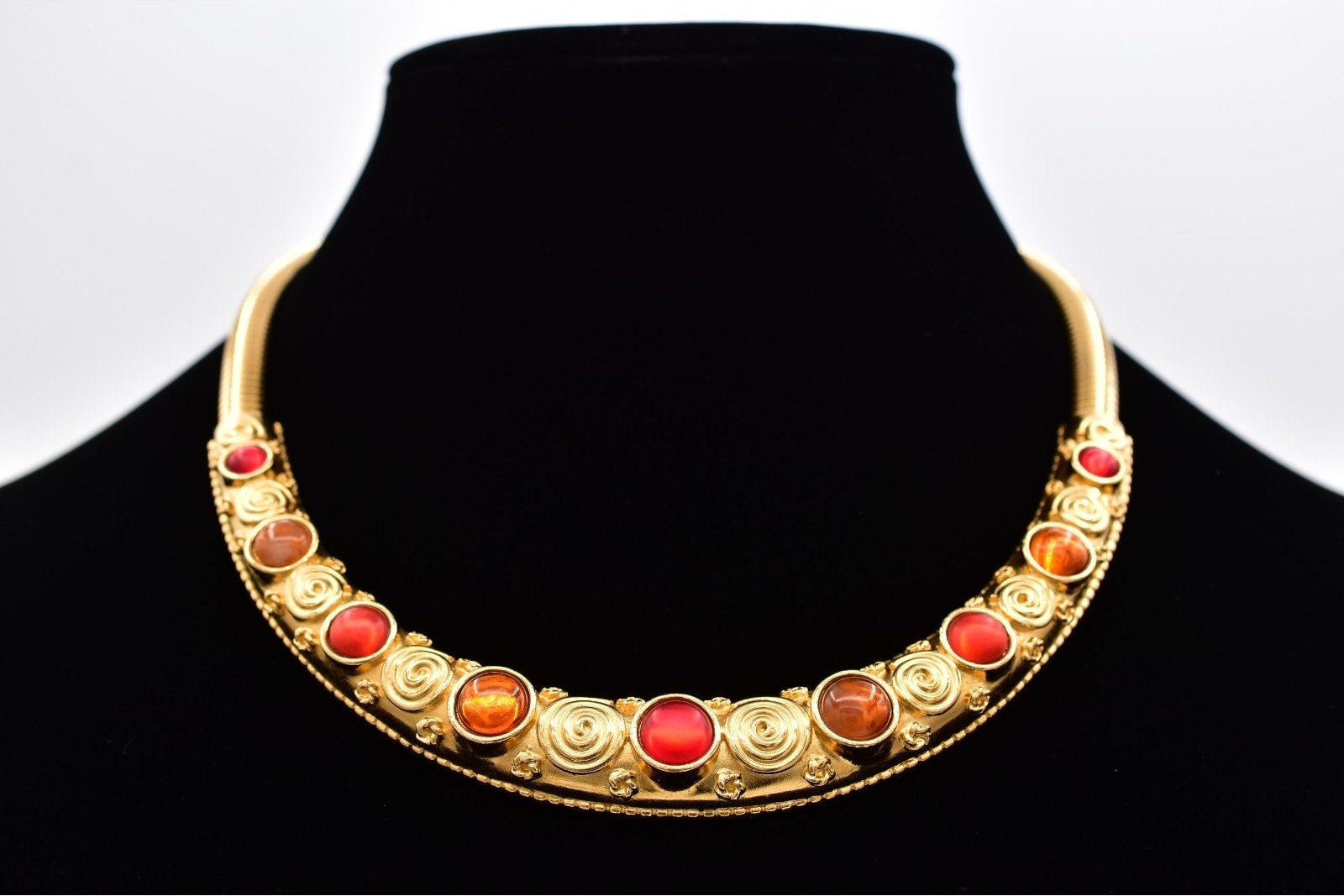 Gold necklace with red and orange stones on a black mannequin against a white background