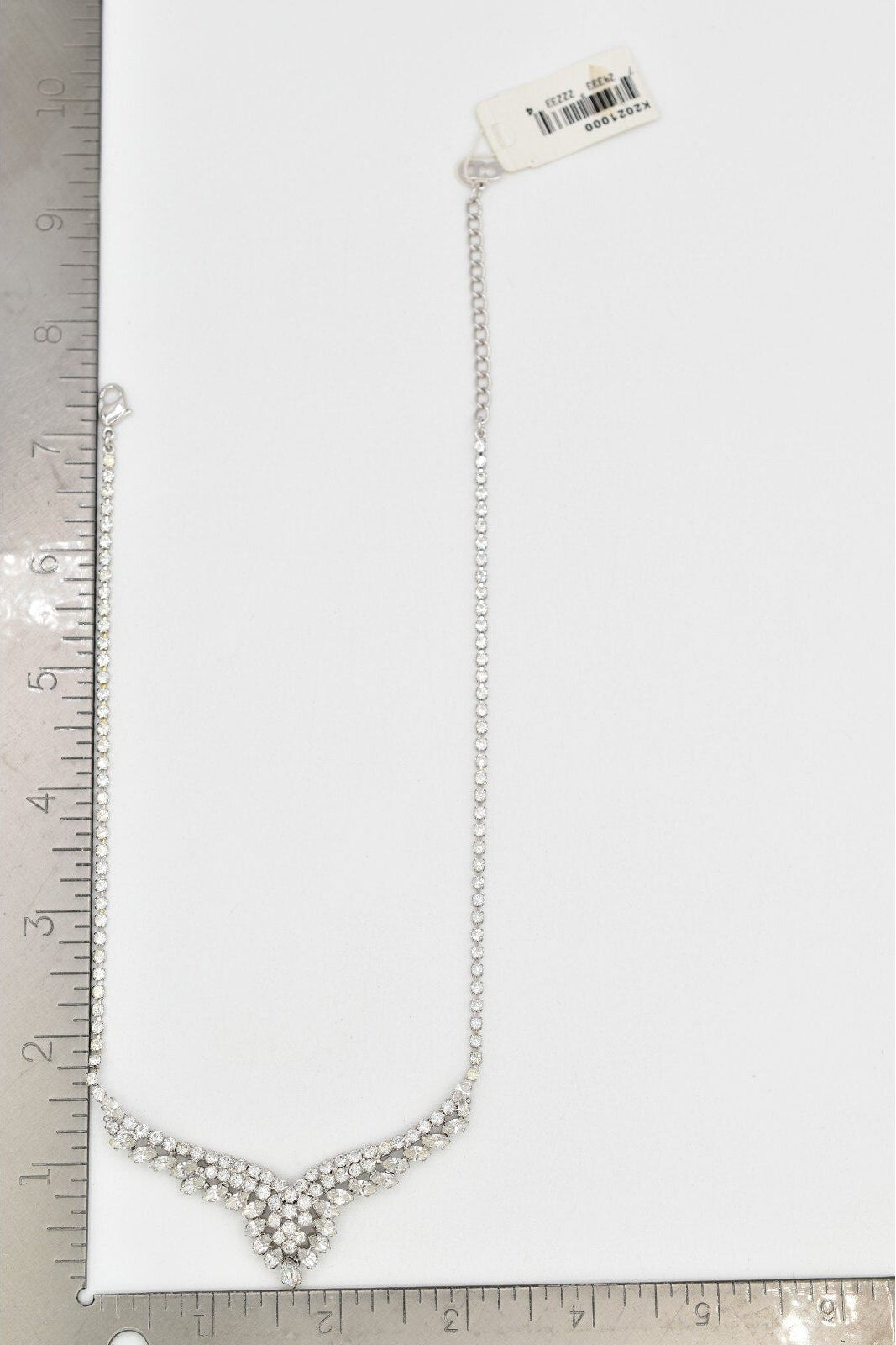 Silver necklace with a heart pendant on a white background with a ruler for scale.