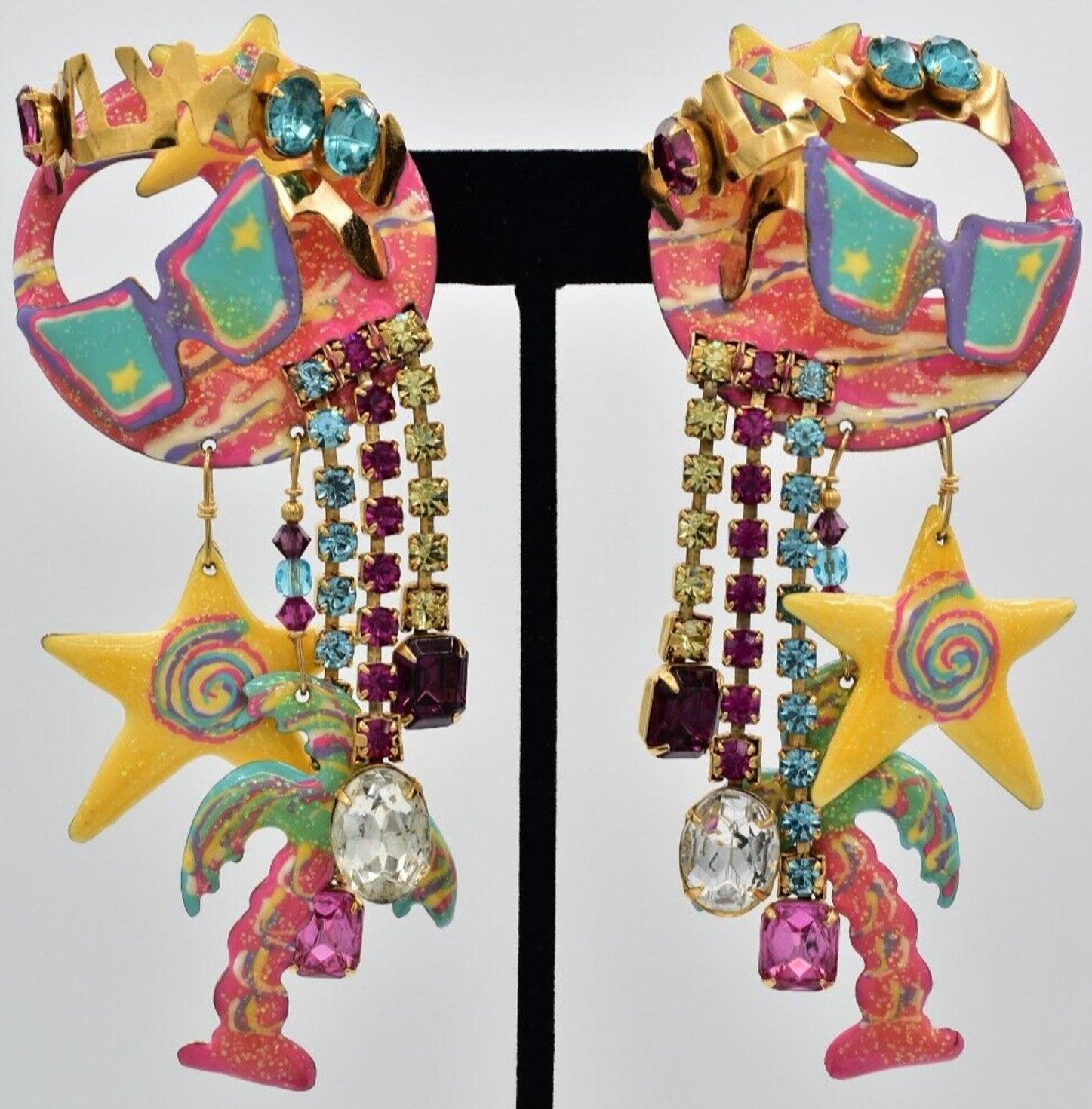 A pair of vintage clip-on earrings featuring a colorful, abstract design with dangling rhinestones.