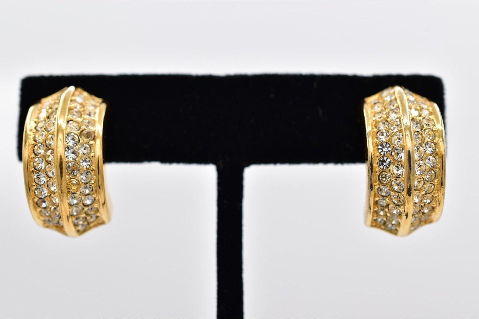 Gold hoop earrings with embedded stones on a black and white display stand.