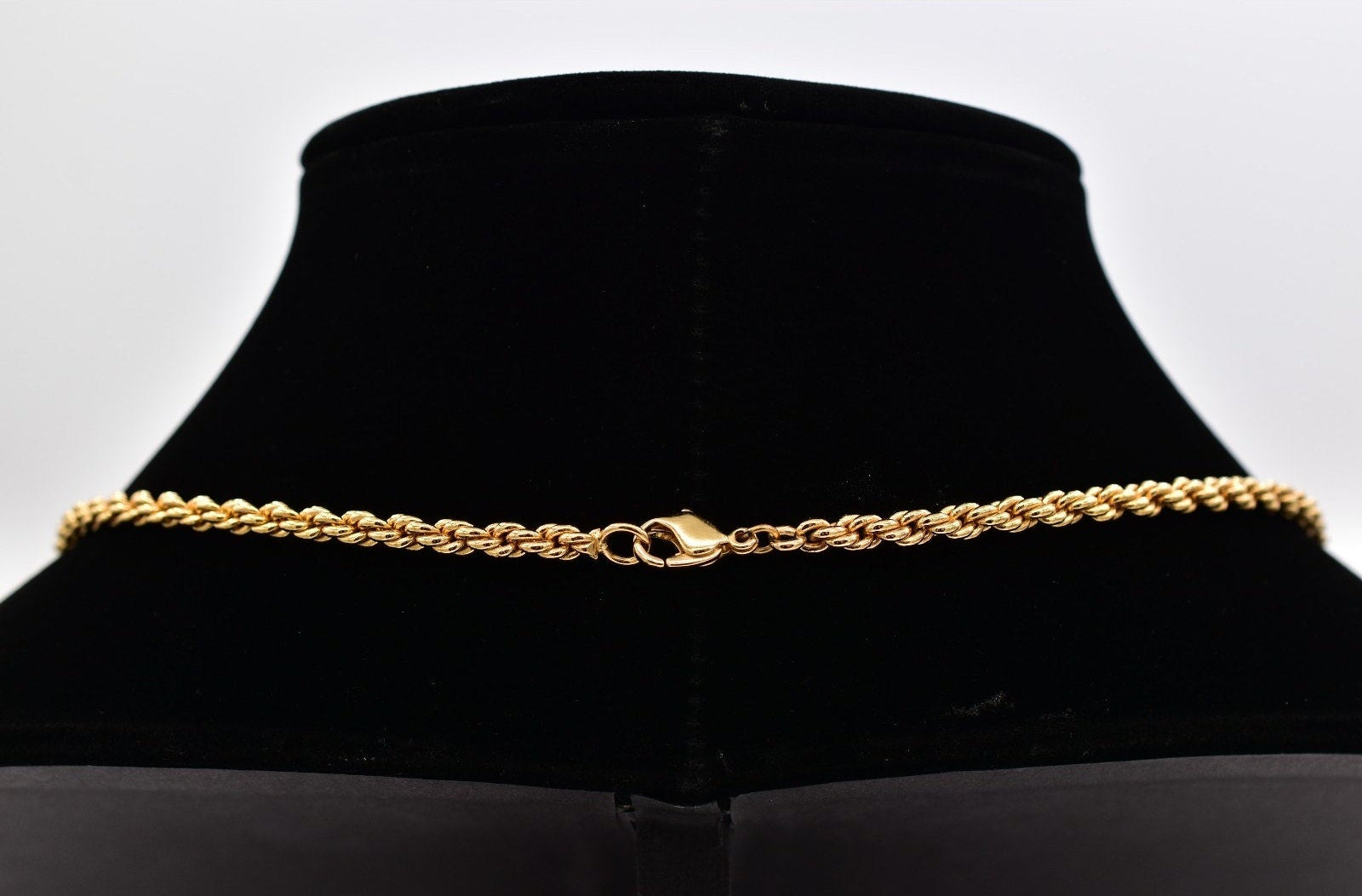 Gold chain necklace on a black mannequin bust against a white background