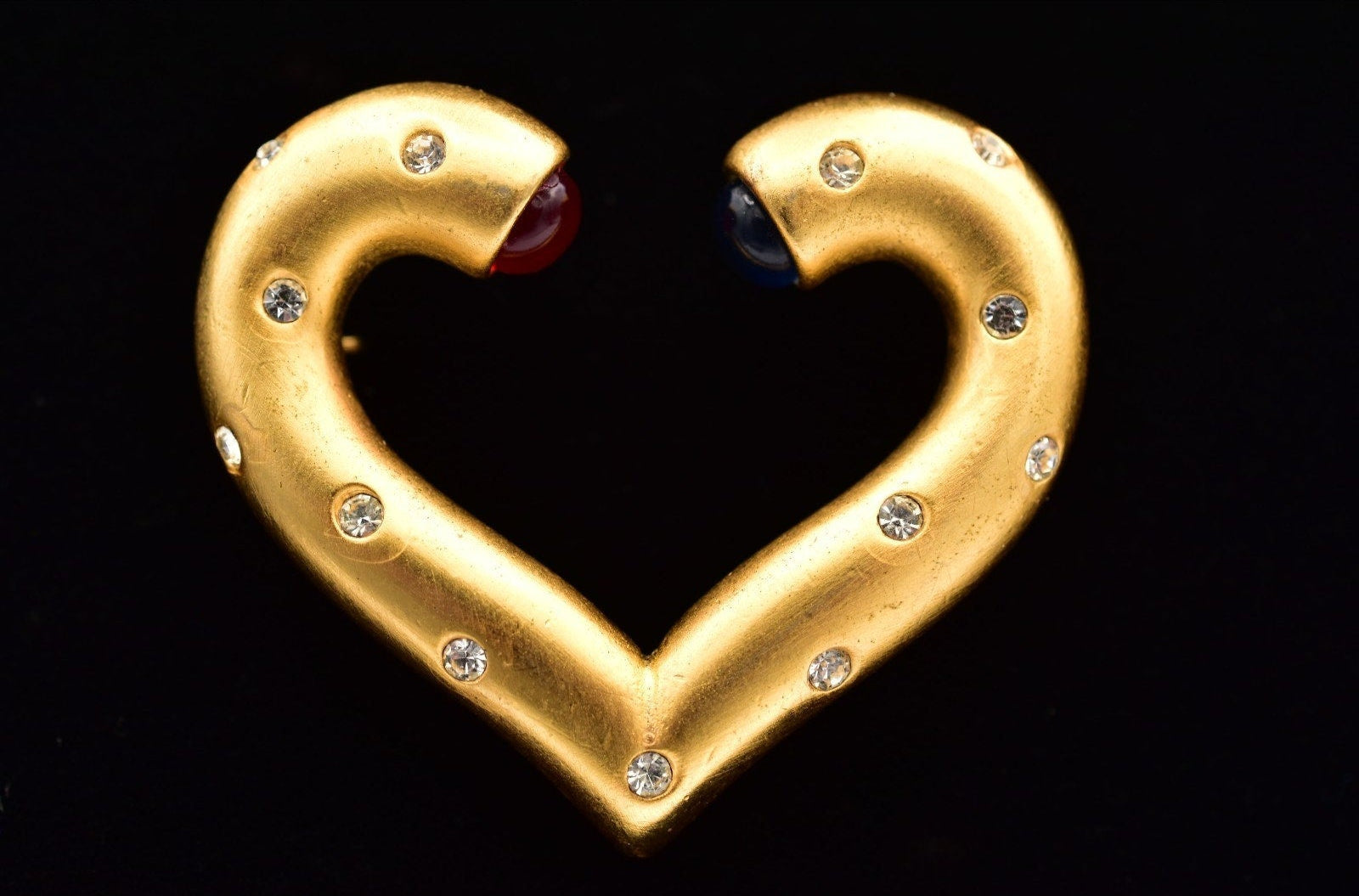 Gold heart-shaped brooch with gemstones on a black background