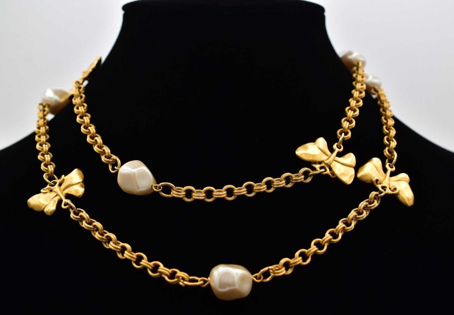 Gold necklace with butterflies and pearl-like beads on a black mannequin.