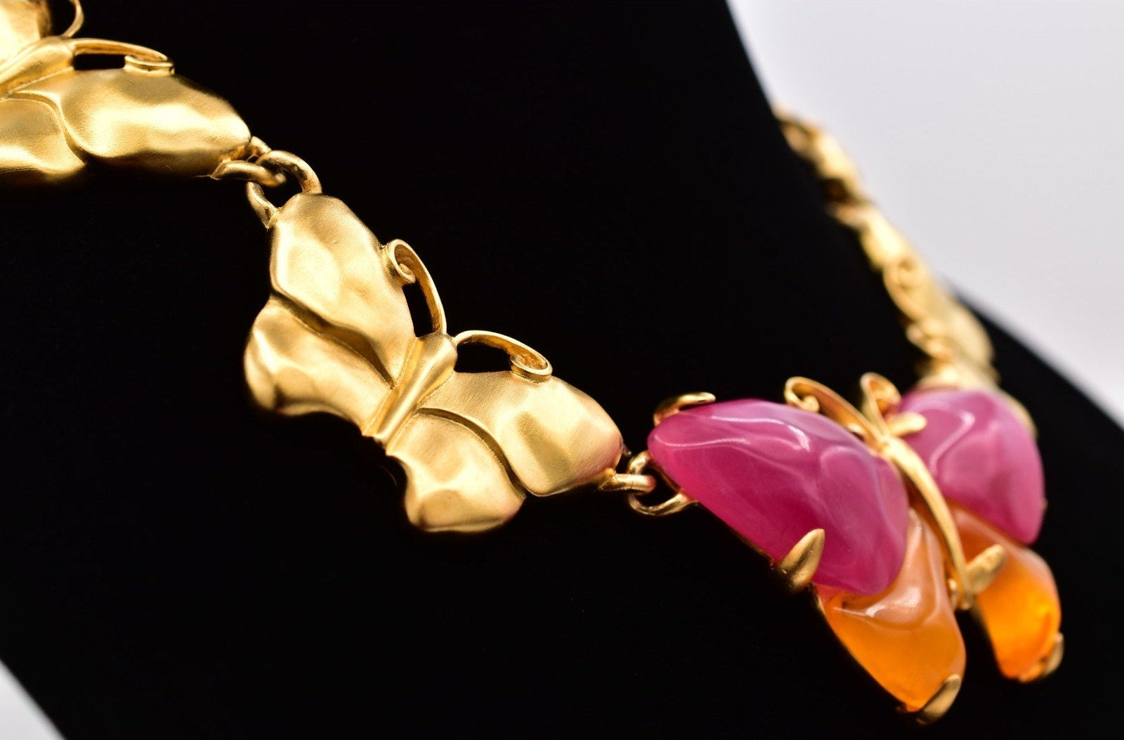 Gold butterfly-shaped necklace with pink and orange stones on a black background