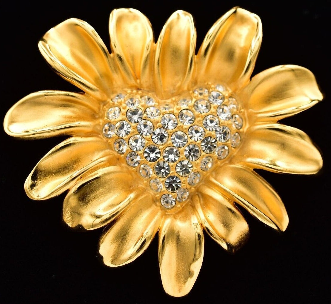 Gold Givenchy flower-shaped brooch with a heart center and clear stones on a black background