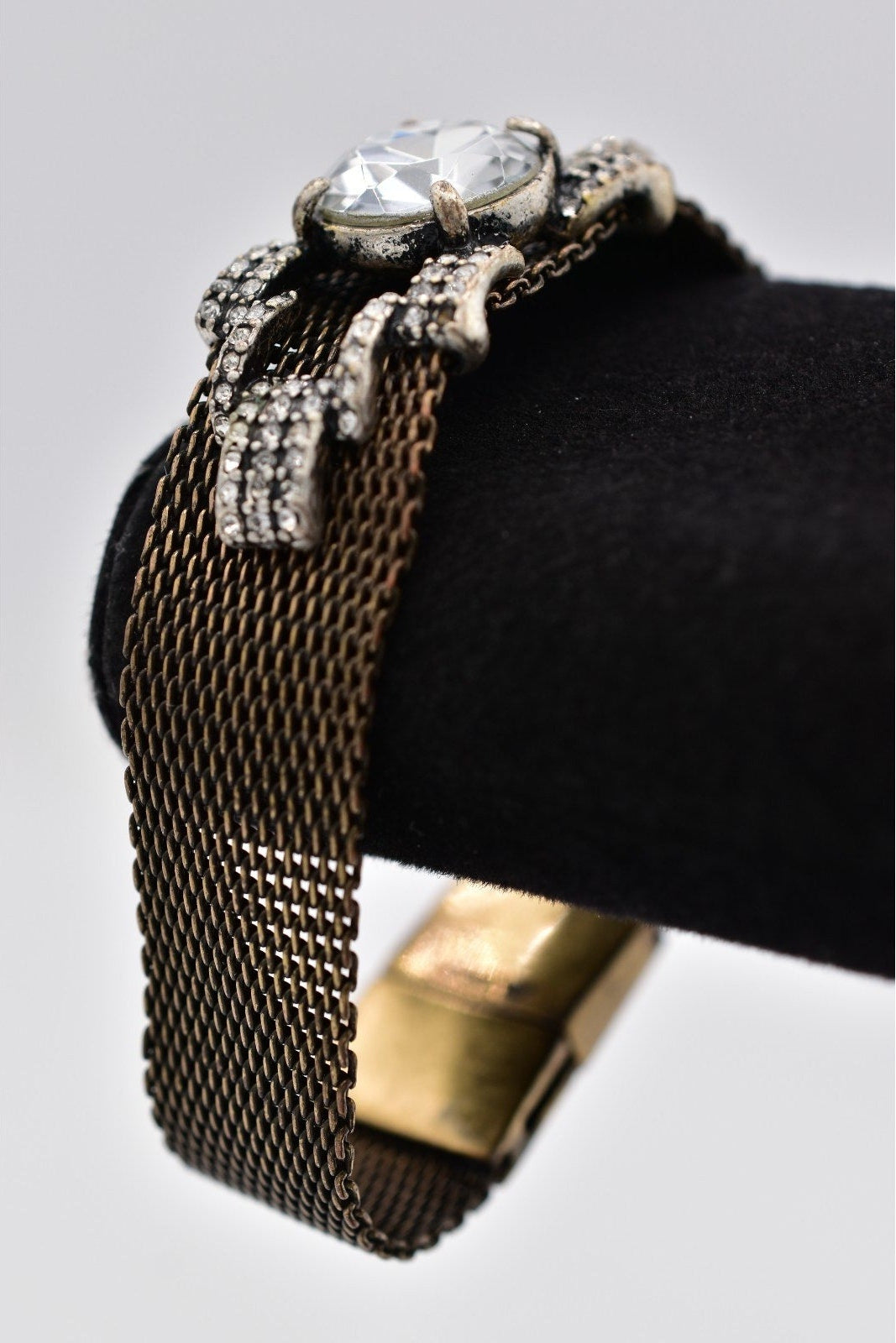 Vintage-style gold bracelet with mesh design and decorative clasp on a black stand.