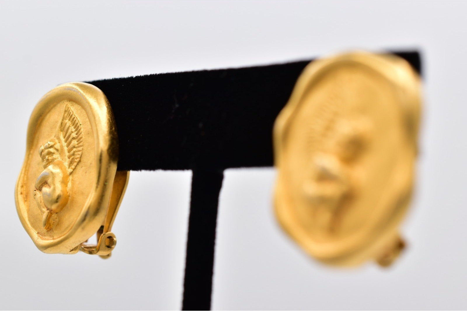 Gold earrings on a black and white stand against a light gray background