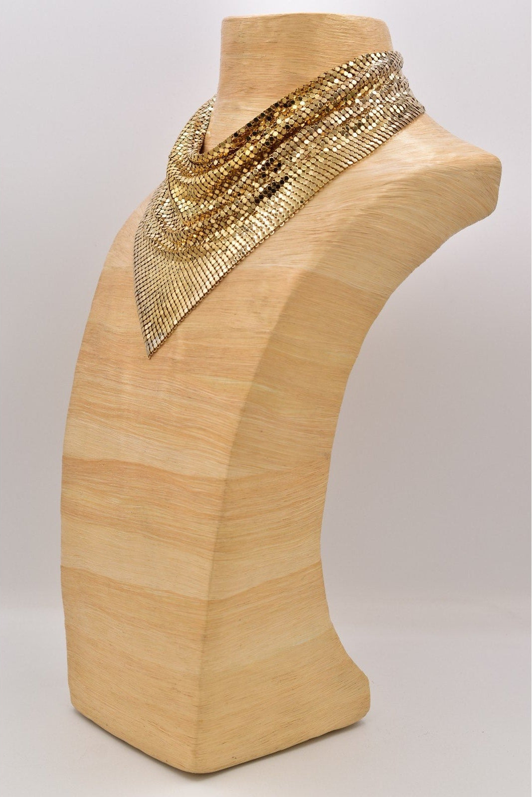 Gold beaded necklace on a wooden mannequin bust against a white background