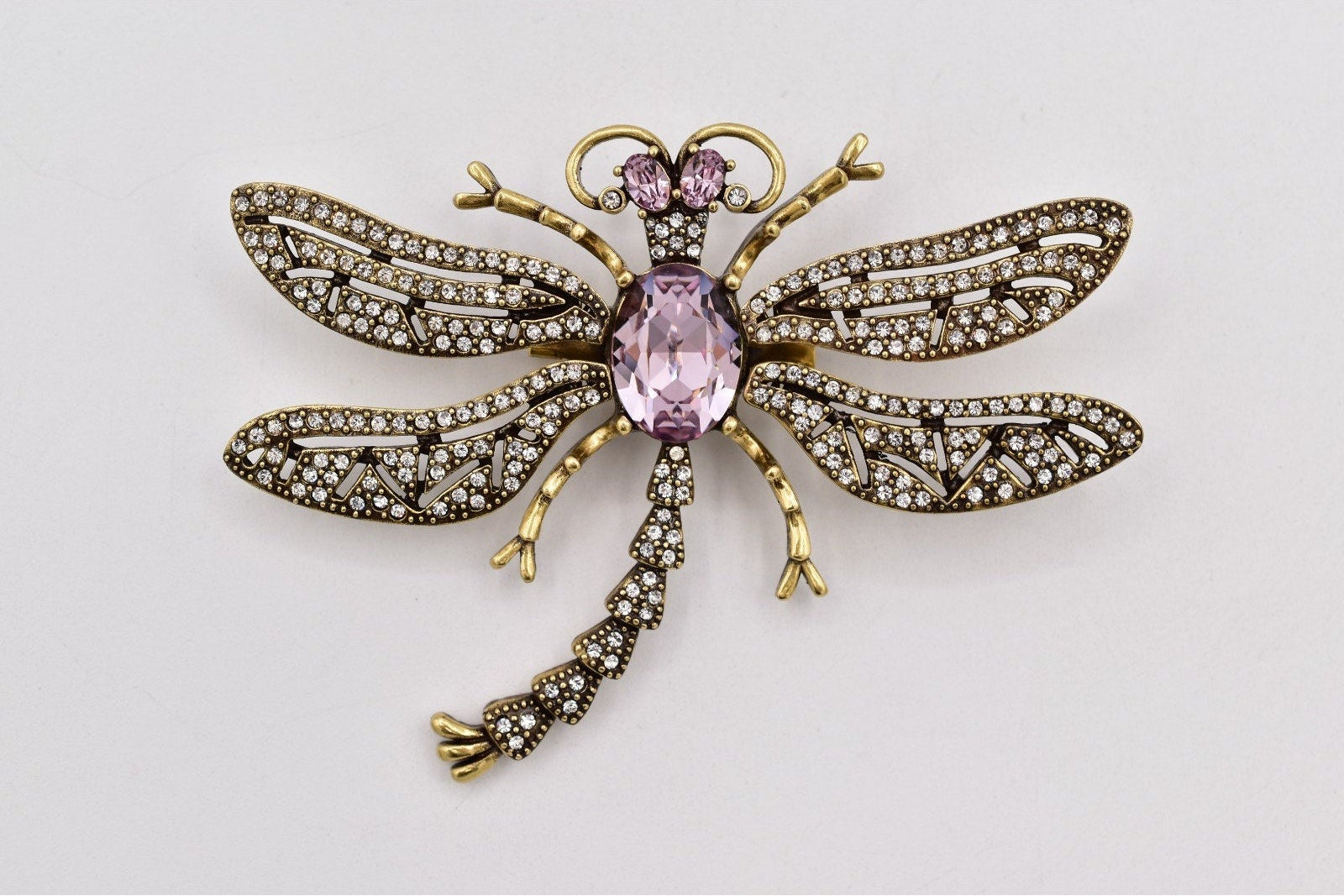 Decorative dragonfly brooch with pink gemstone on a light gray background