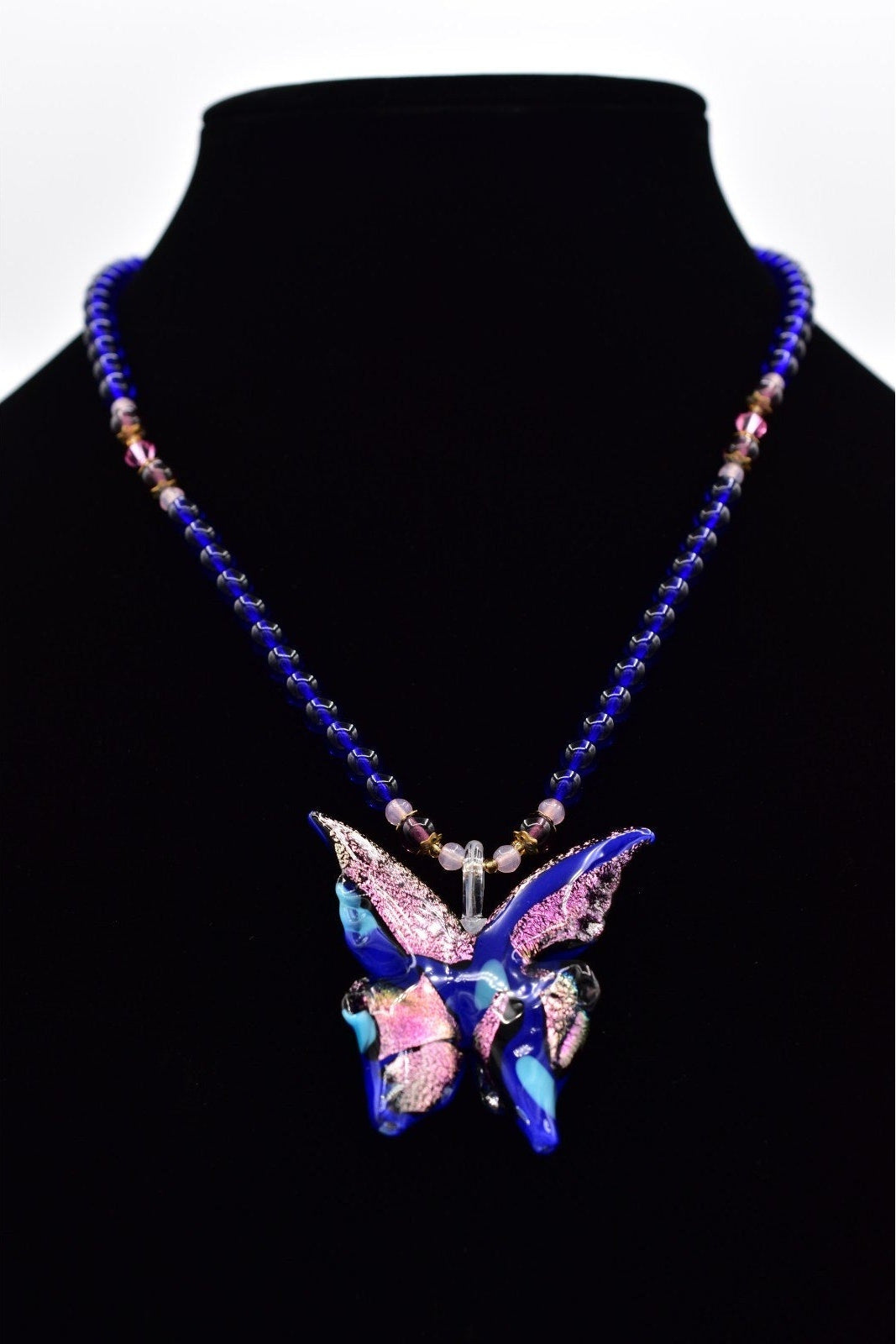 Necklace with a butterfly pendant on a black stand against a white background