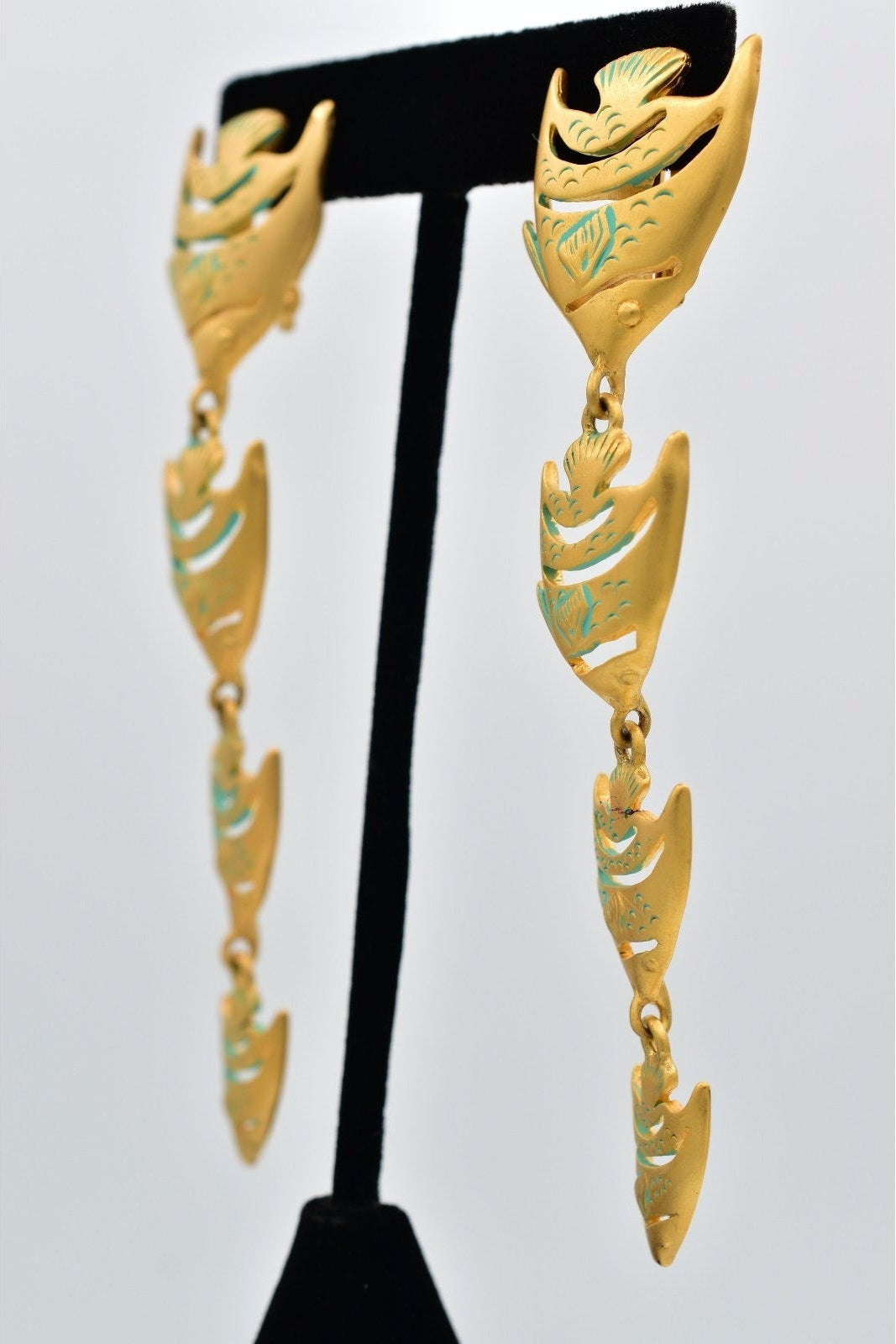 Gold and green Givenchy fish-shaped earrings on a black earring stand against a white background