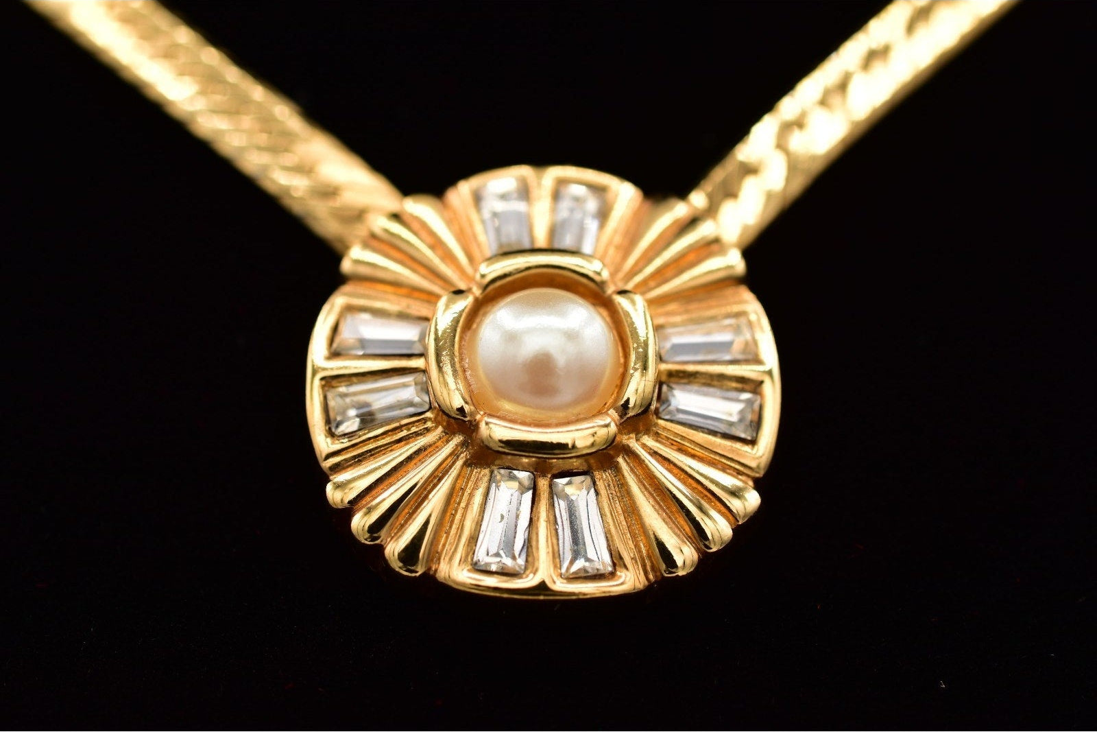 Gold necklace with a central pearl and diamond-like stones on a black background