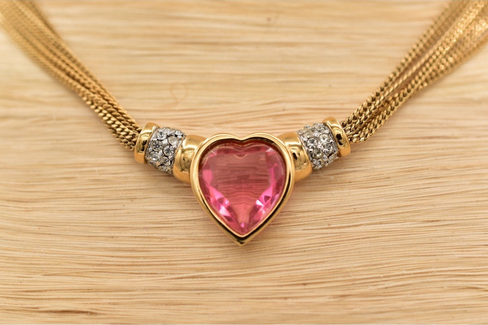 Gold necklace with a pink heart-shaped gemstone on a wooden surface