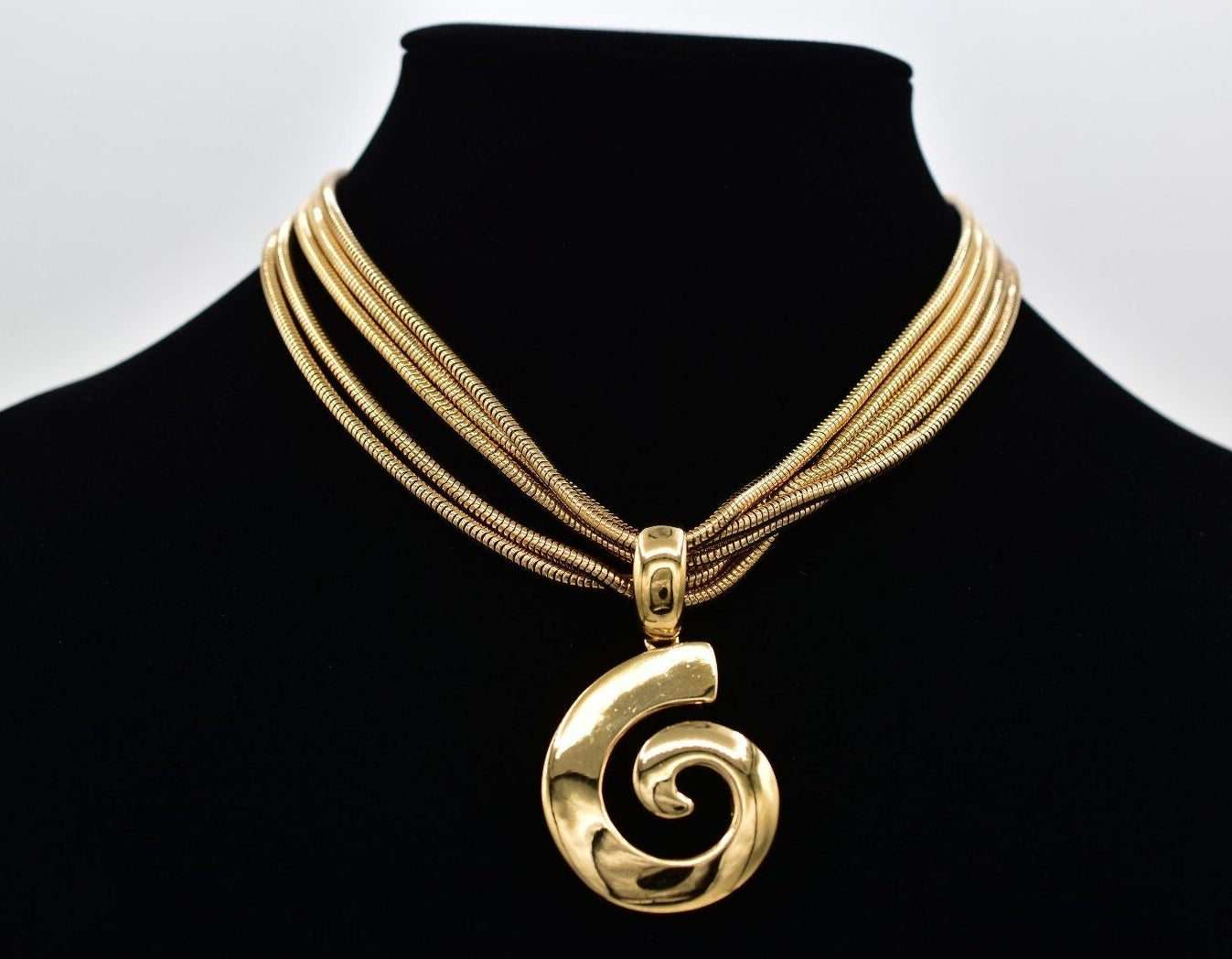 Gold necklace with a spiral pendant on a black mannequin against a white background