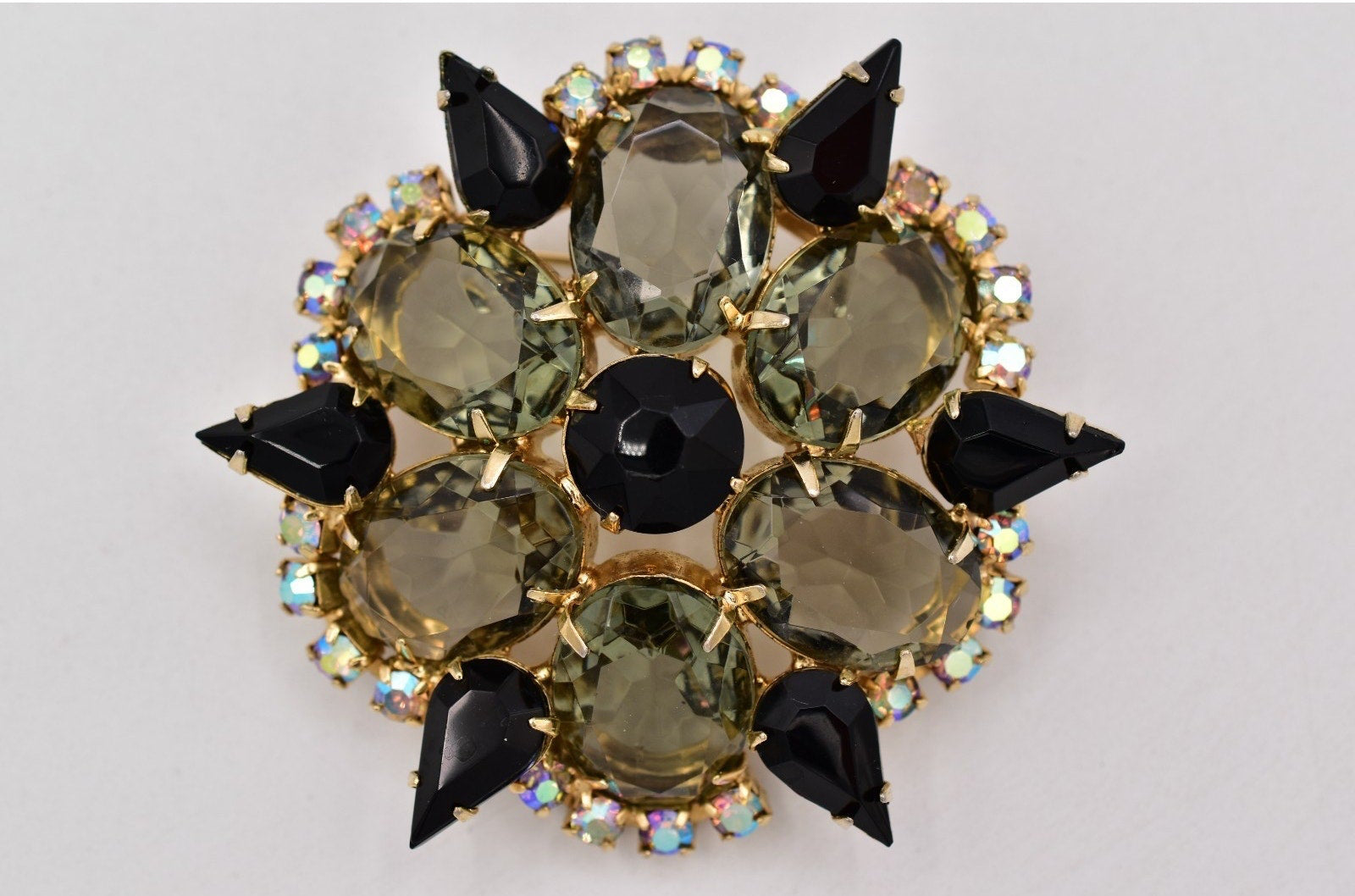 Decorative brooch with green gemstones and black accents on a light gray background