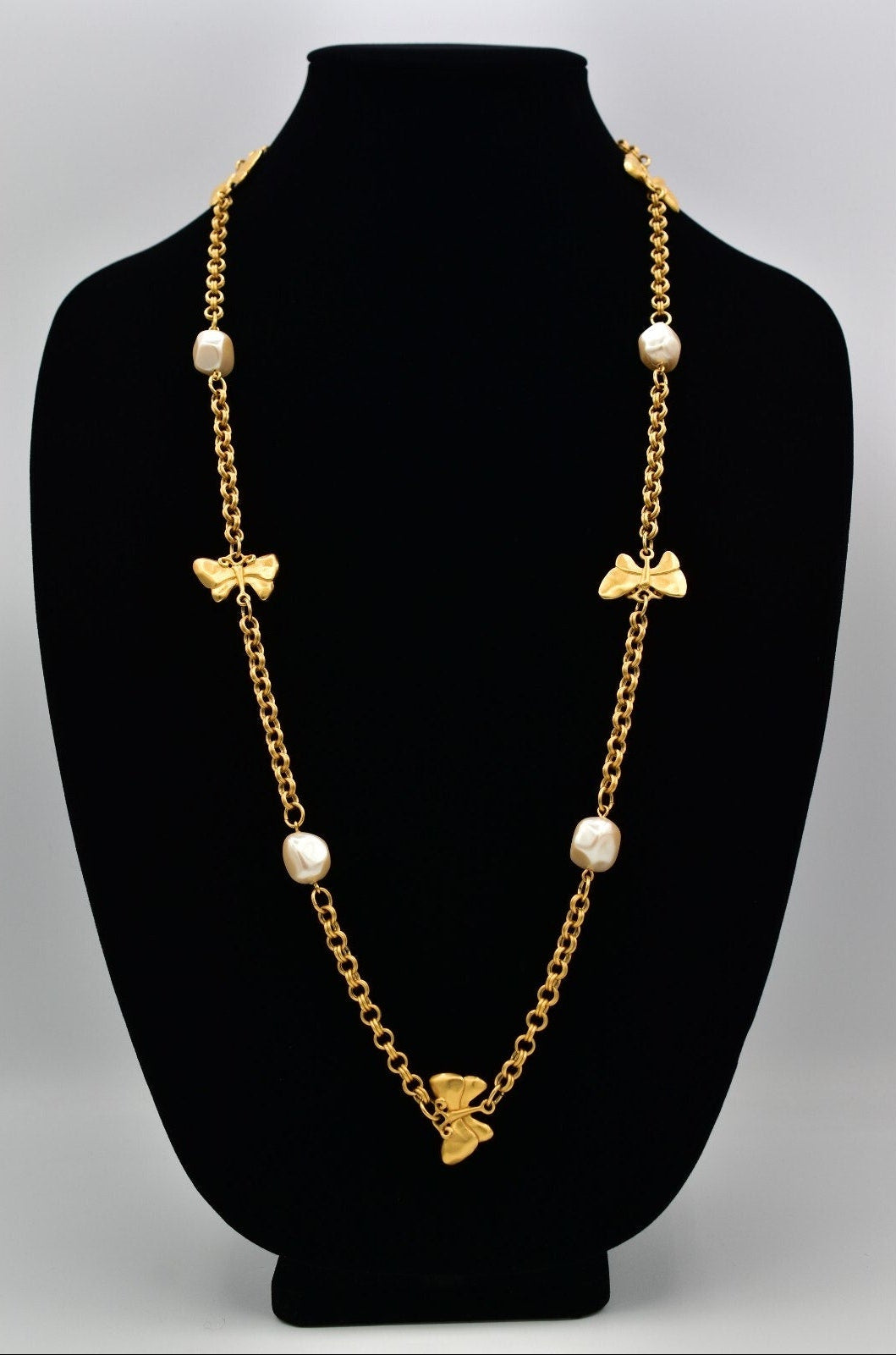 Gold chain necklace with butterflies and pearl beads on a black mannequin bust.