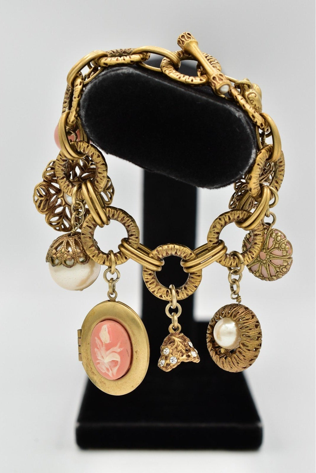 Gold charm bracelet with various charms on a black stand against a light gray background