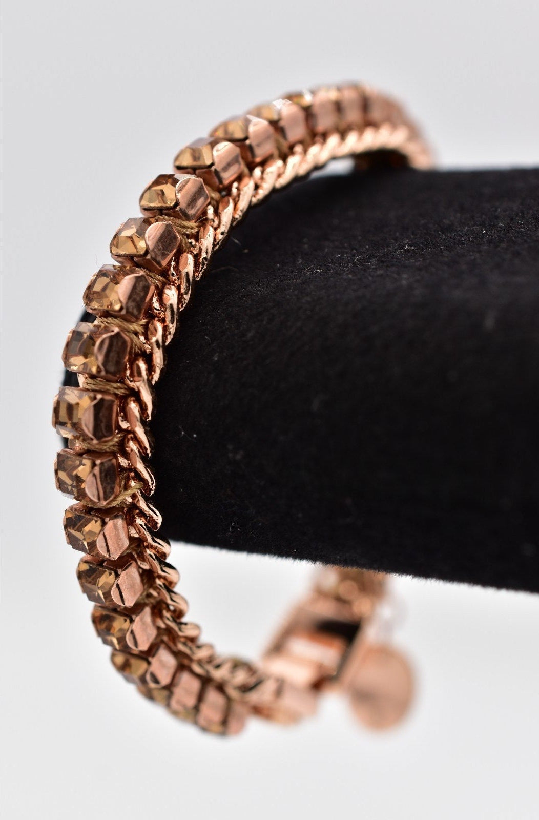 Rose gold bracelet on a black stand against a light gray background