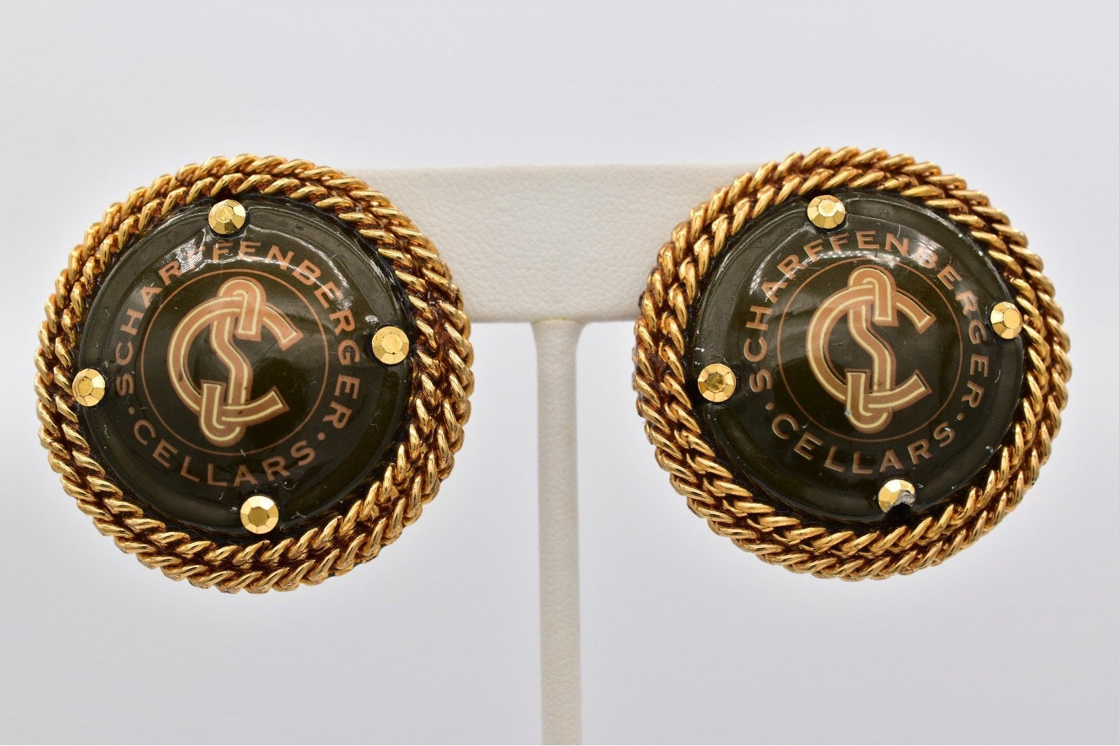 Pair of gold and black Schaeffenberger Cellars earrings on a white stand.