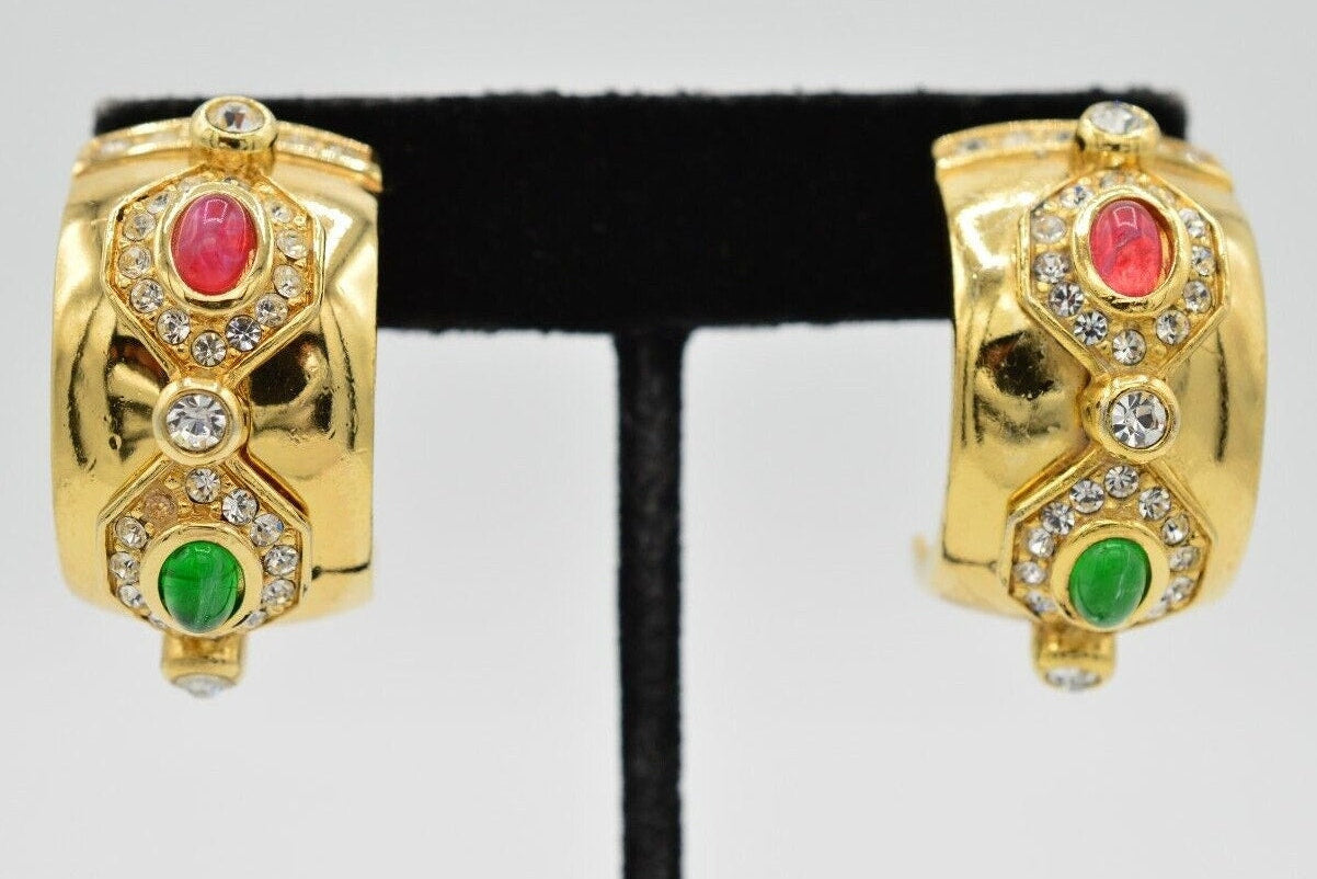 Gold hoop earrings with red and green gemstones on a black stand.