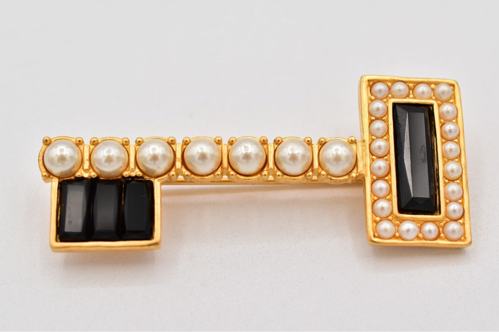 Gold brooch with pearls and black stones on a light gray background