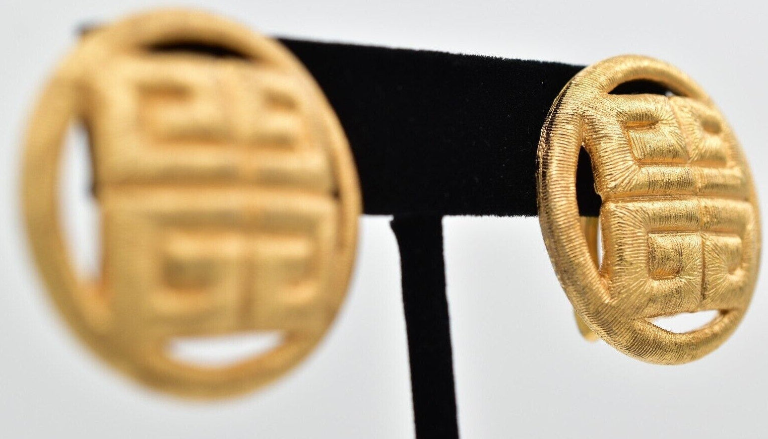 Pair of gold earrings on a black stand against a light gray background