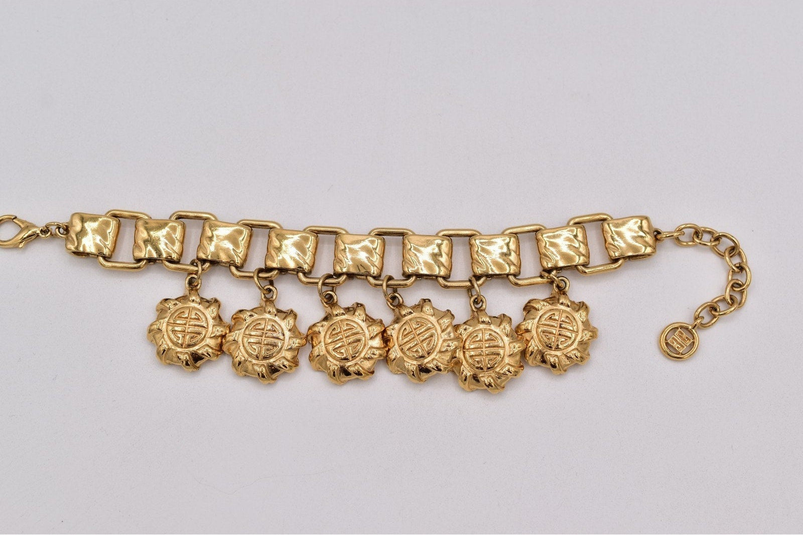 A gold-tone chain bracelet featuring textured rectangular links and five dangling circular medallion charms, displayed on a light gray background.
