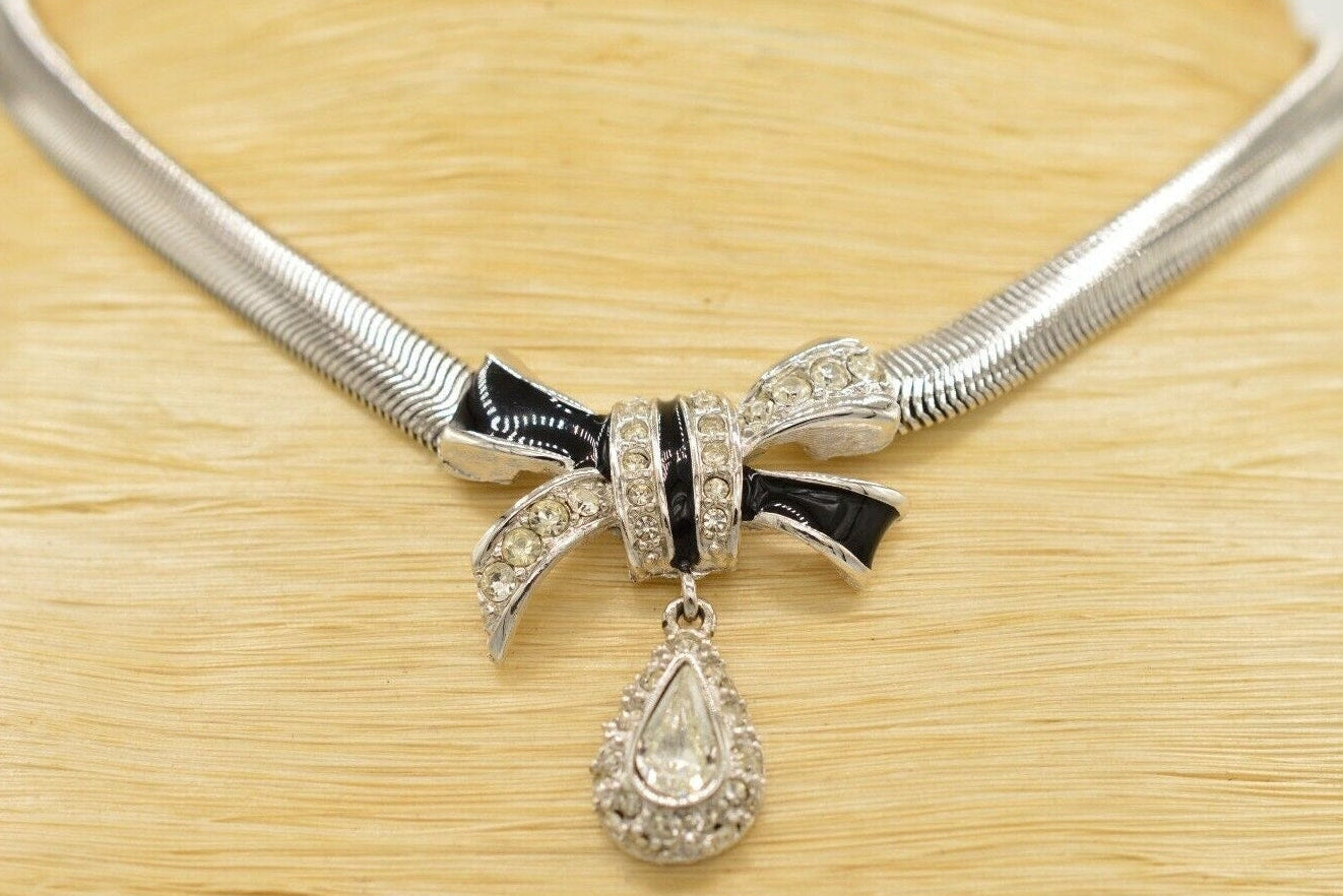 Silver necklace with bow and teardrop pendant on a wooden surface