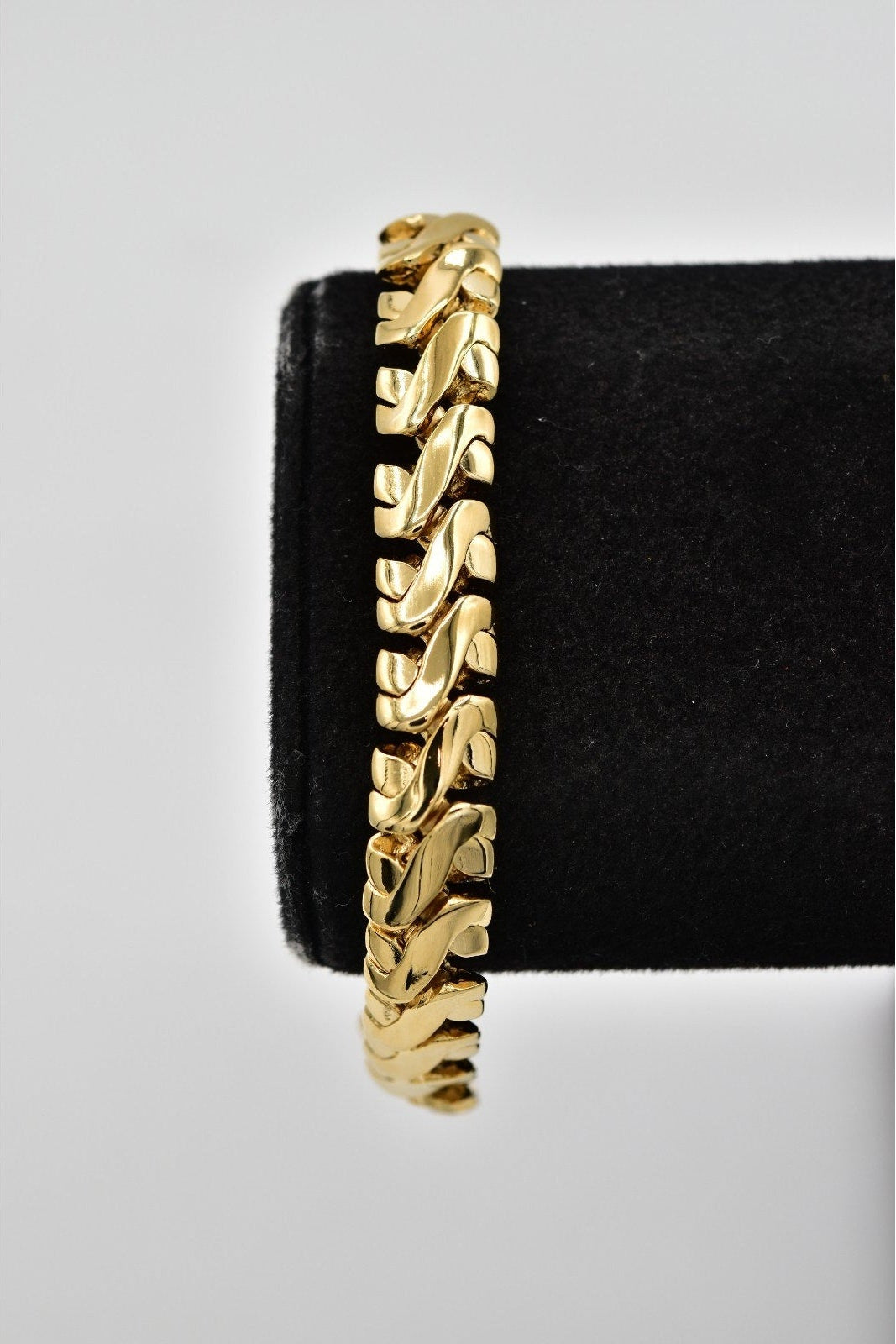 A polished gold-tone chain link bracelet displayed on a black velvet jewelry stand against a light gray background.