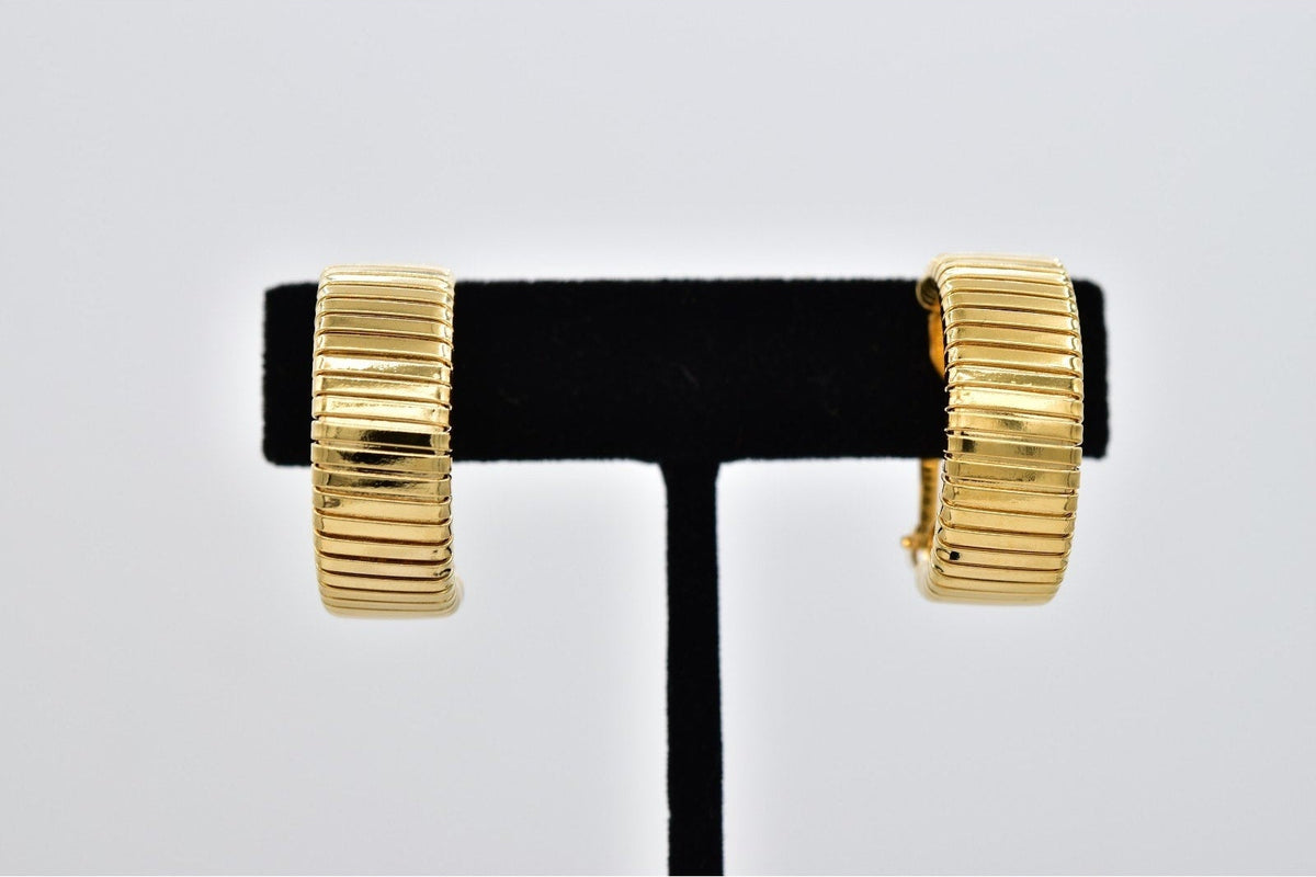 A pair of gold-plated ribbed hoop earrings displayed on a black velvet jewelry stand against a light gray background.