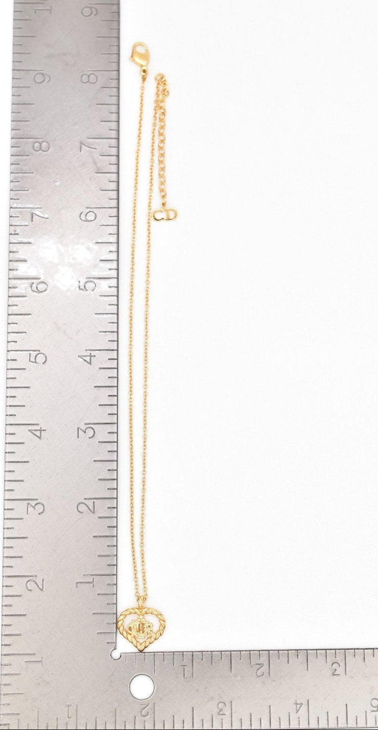 Gold necklace with heart pendant next to a ruler on a white background