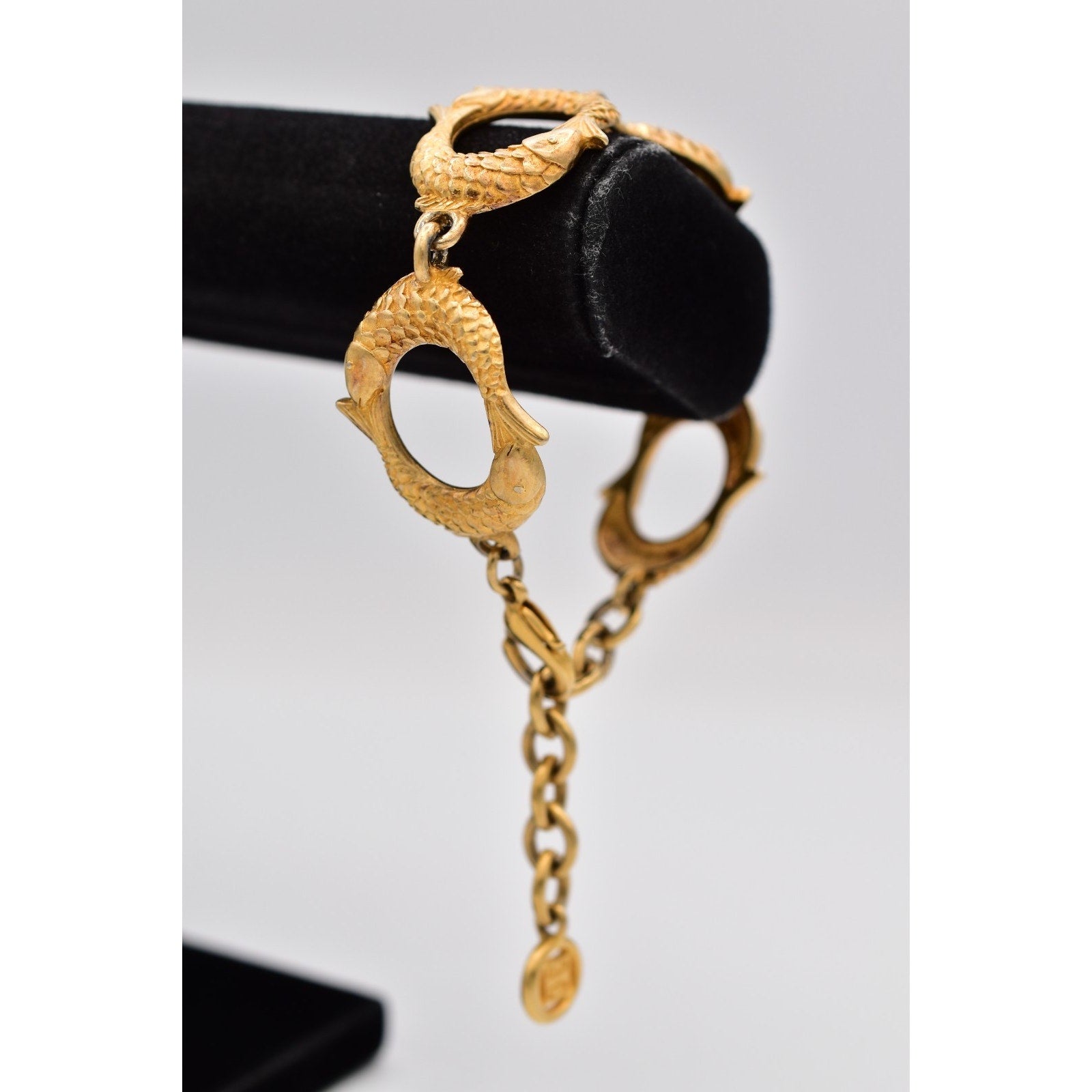 Gold bracelet with intricate design on a black stand against a light gray background