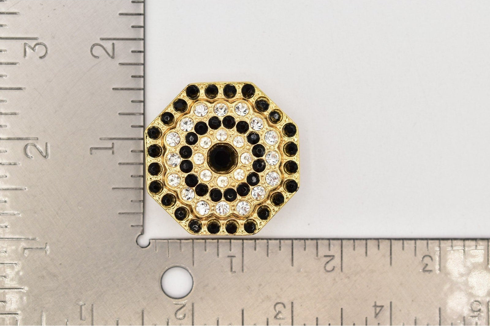 Decorative circular object with black and gold design next to a ruler for scale.