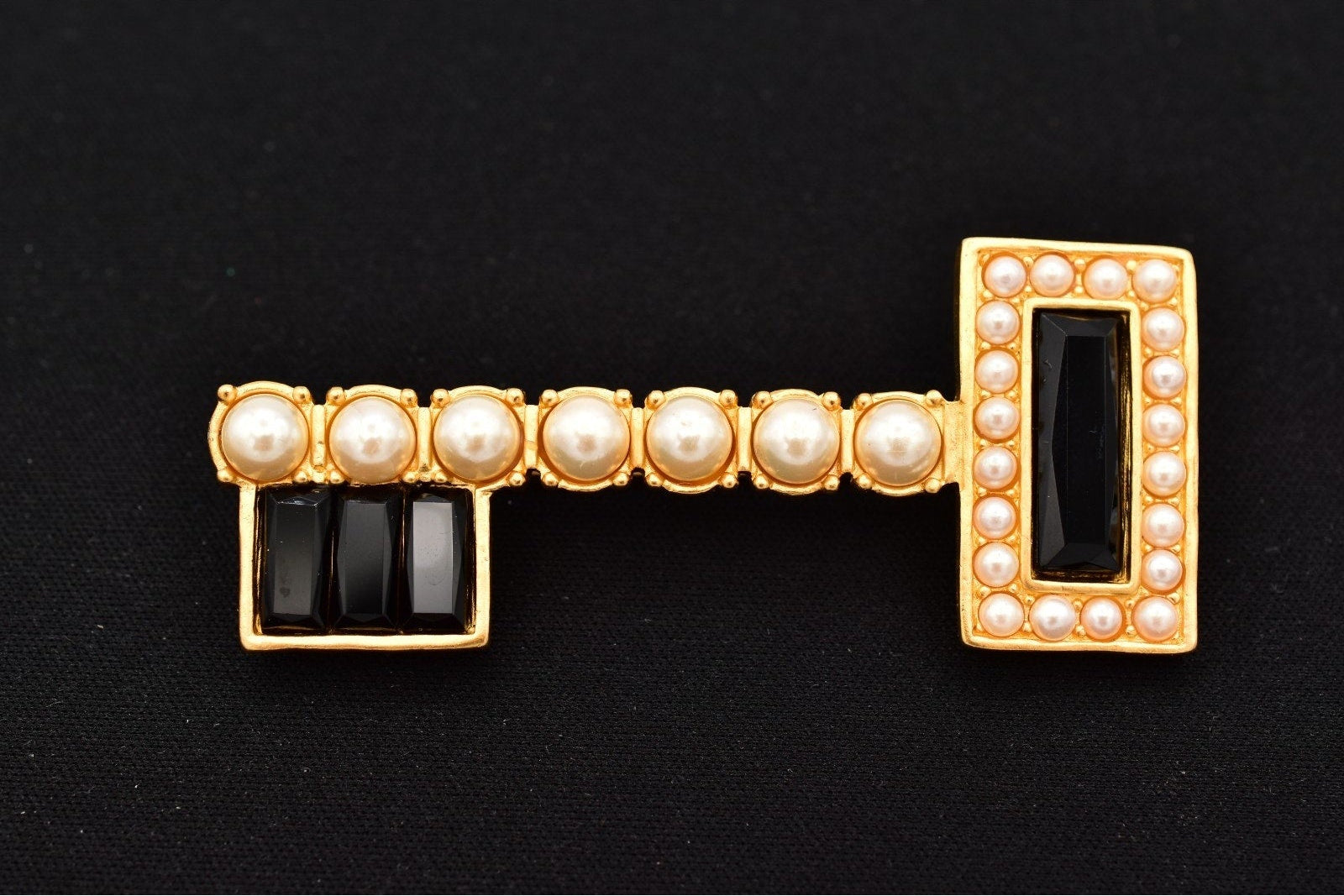 Gold key-shaped brooch with pearls and black stones on a black background