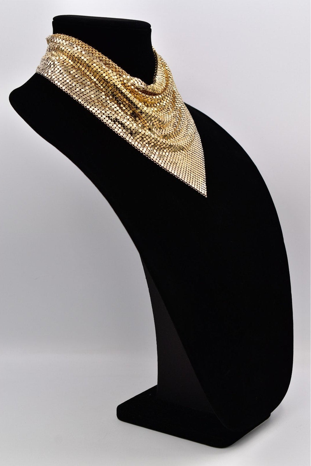Gold beaded necklace on a black mannequin bust against a white background
