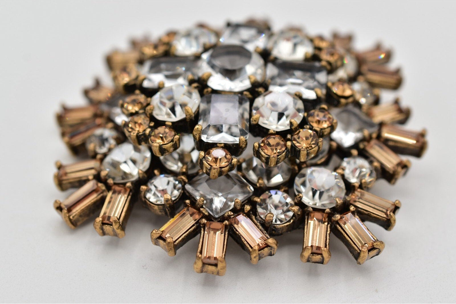 Decorative brooch with gold and clear gemstones on a light gray background