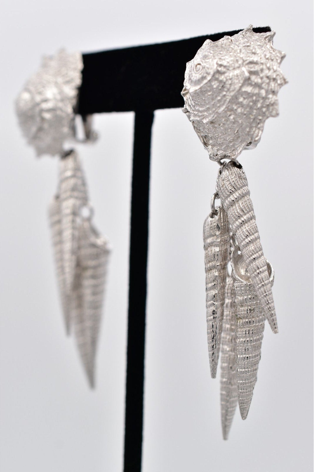 Pair of silver earrings on a black stand against a white background