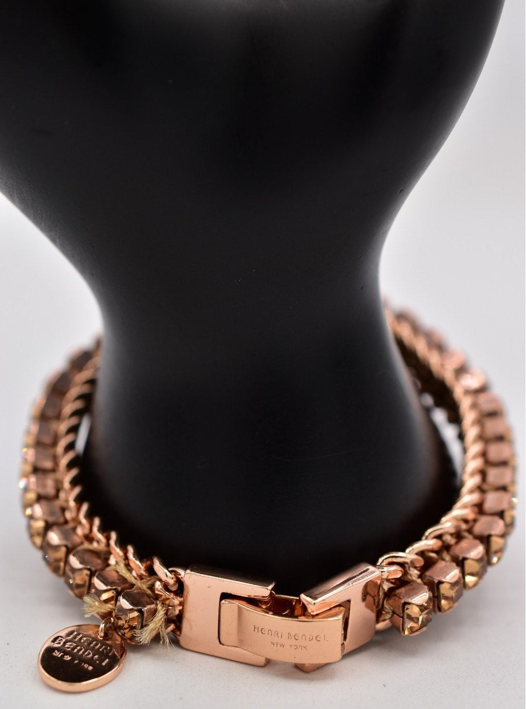 Rose gold bracelet with a clasp and tag on a black mannequin bust.