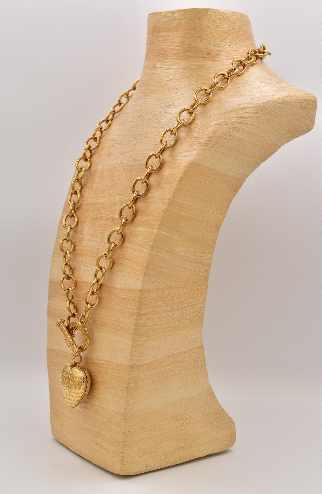 Gold chain necklace on a wooden mannequin bust with a plain background