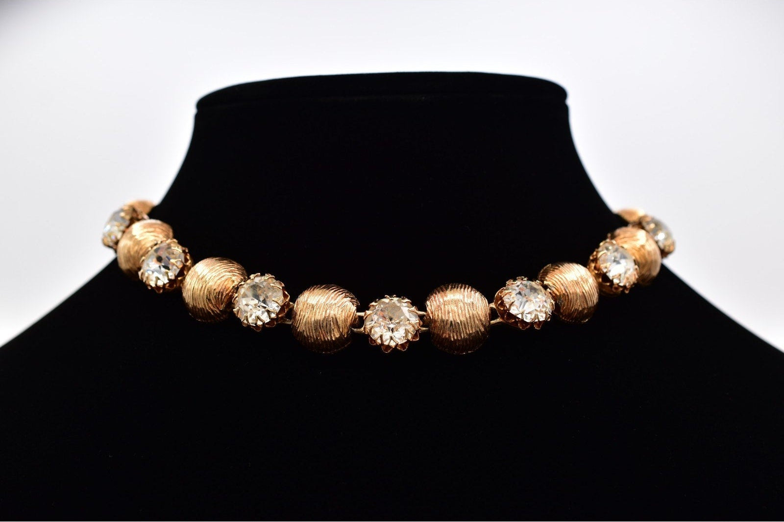 Gold and crystal necklace on a black mannequin bust against a white background