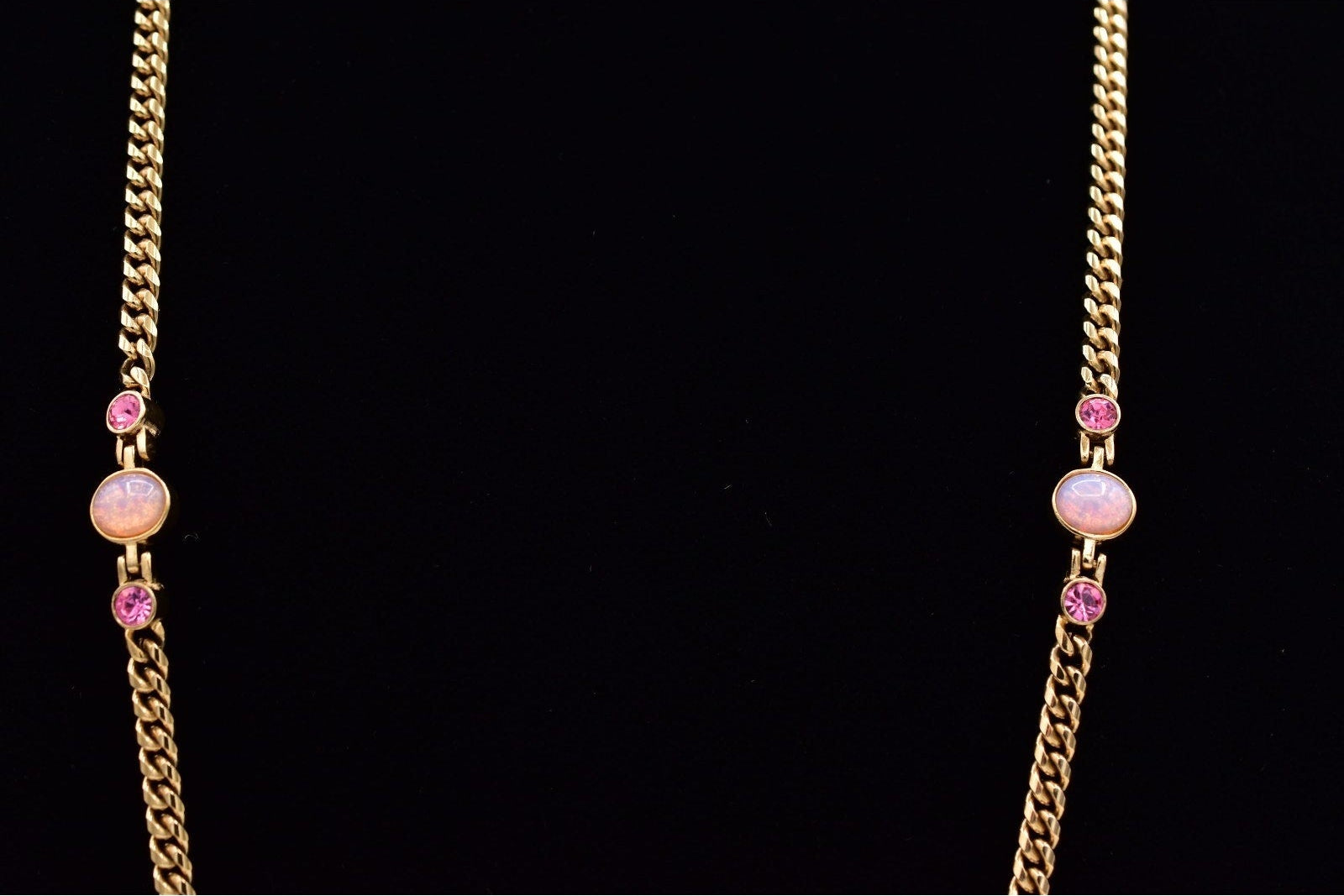 A gold chain necklace featuring oval pinkish-white opal-like beads and small round pink gemstones, displayed against a solid black background.
