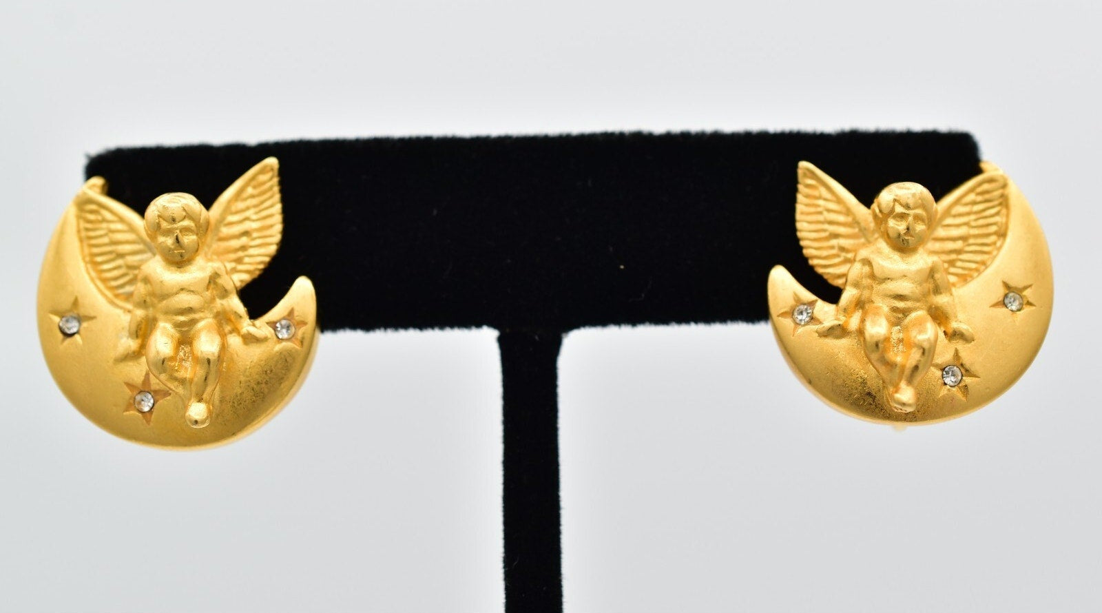 Gold angel earrings on a black stand against a light gray background