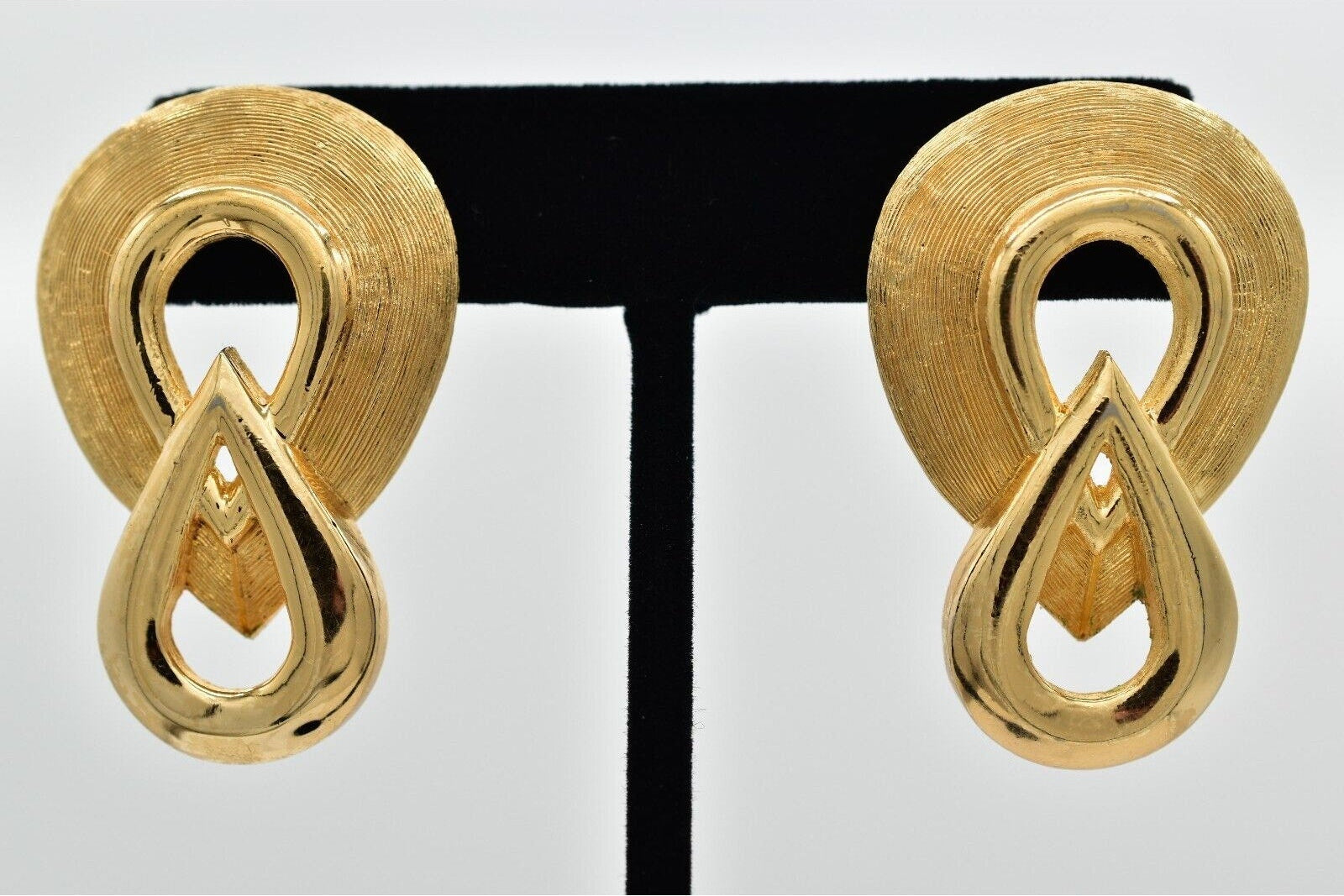Pair of gold earrings on a black stand with a white background