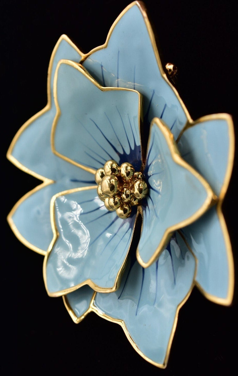 Blue flower-shaped brooch with gold accents on a black background